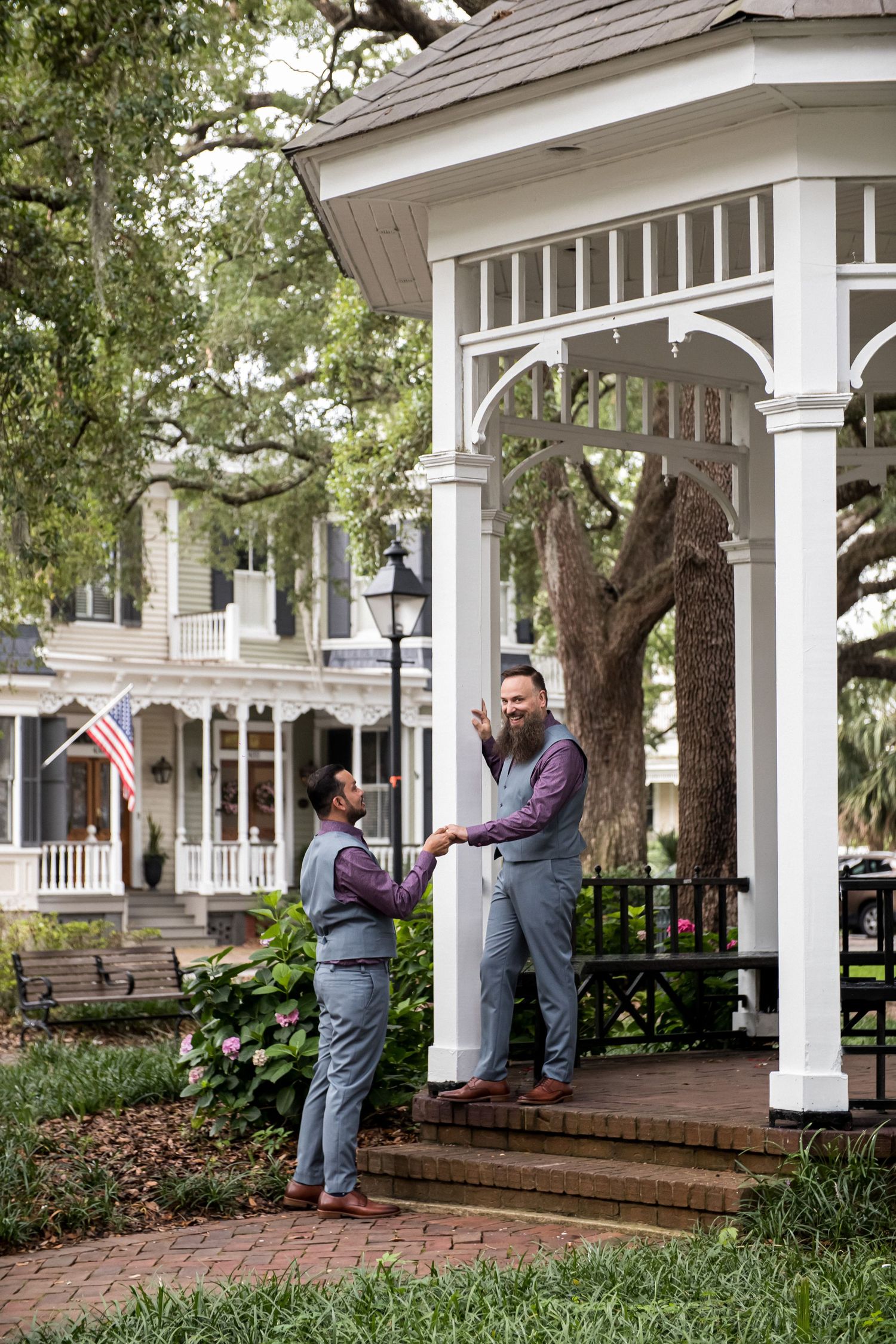 Two people having a conversation on a white porch with brick steps and greenery in the background.