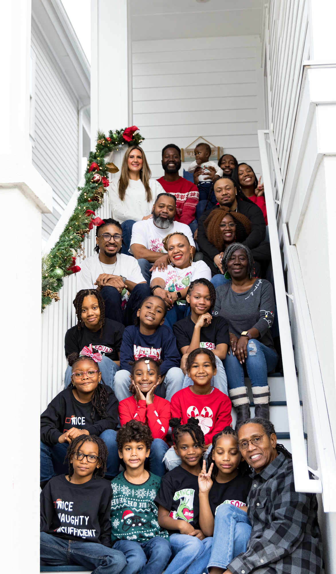 A large family group poses together on white porch steps decorated with holiday greenery and red bows.