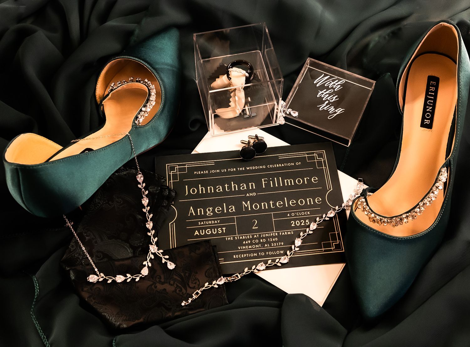 Elegant wedding flat lay with teal heels, black clutch, crystal necklace, and gold wedding invitation on satin fabric.
