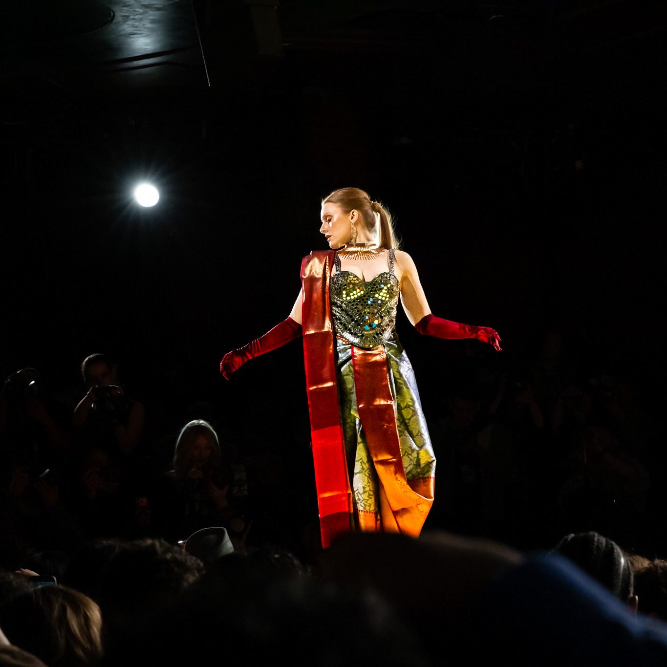 Performer in a glittering dress and red gloves strikes dramatic poses on a dark stage with spotlighting.