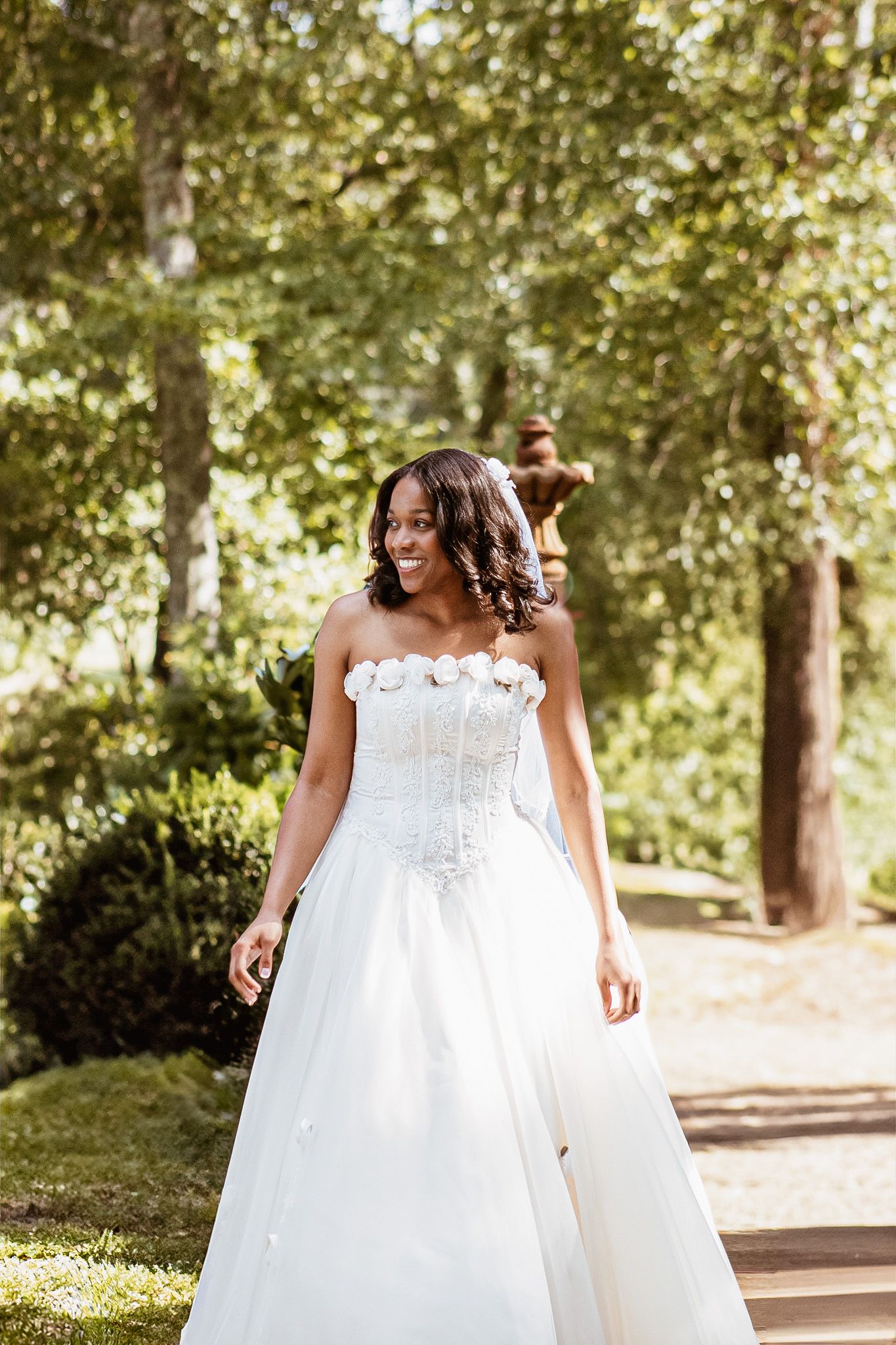 Sunlit garden pathway with trees creating natural frame for bridal portraits.