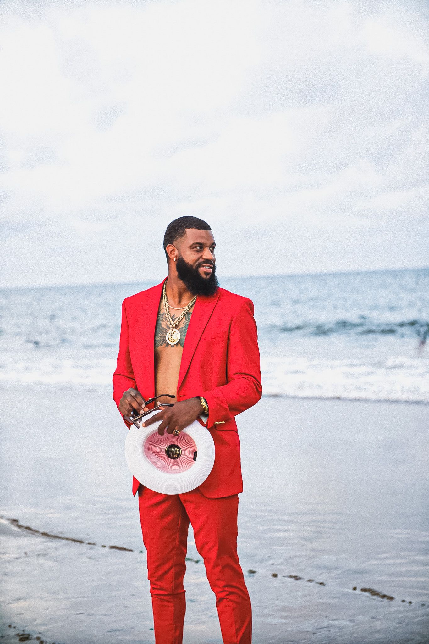 A person in a bright red suit holding a megaphone stands on a beach against an ocean backdrop.
