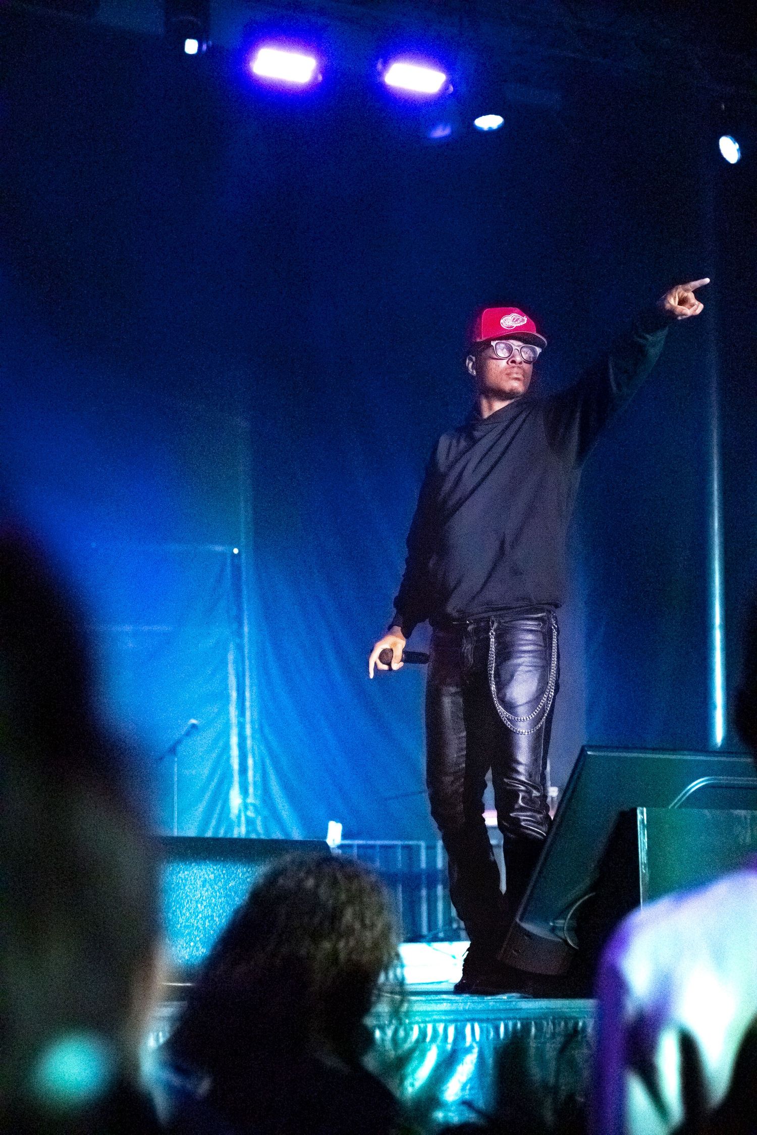 Performer silhouetted on dark stage with dramatic blue lighting and crowd visible in foreground.