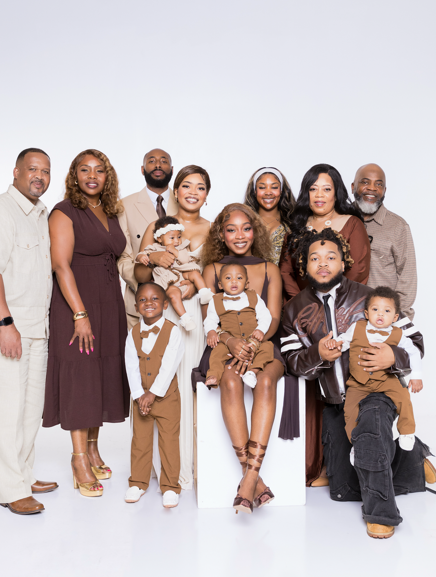 Large family portrait with adults and children posing together in coordinated brown and tan outfits against a white background.