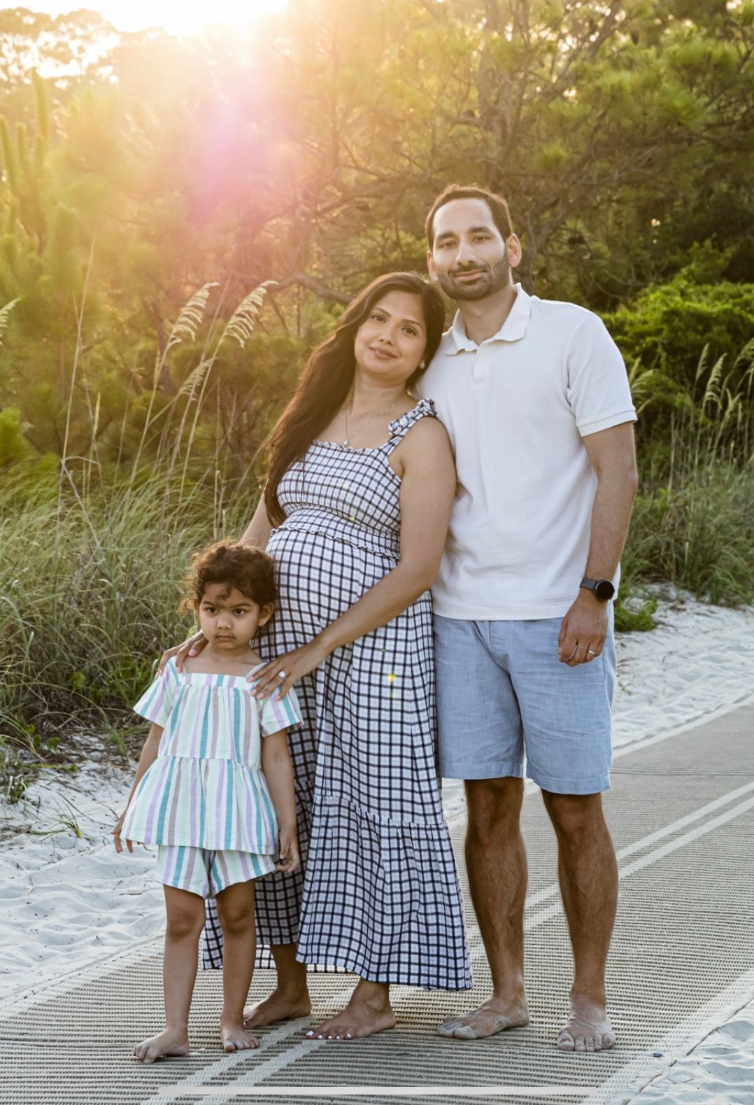 A family poses together on a beach boardwalk at sunset, wearing coordinated blue and white outfits.
