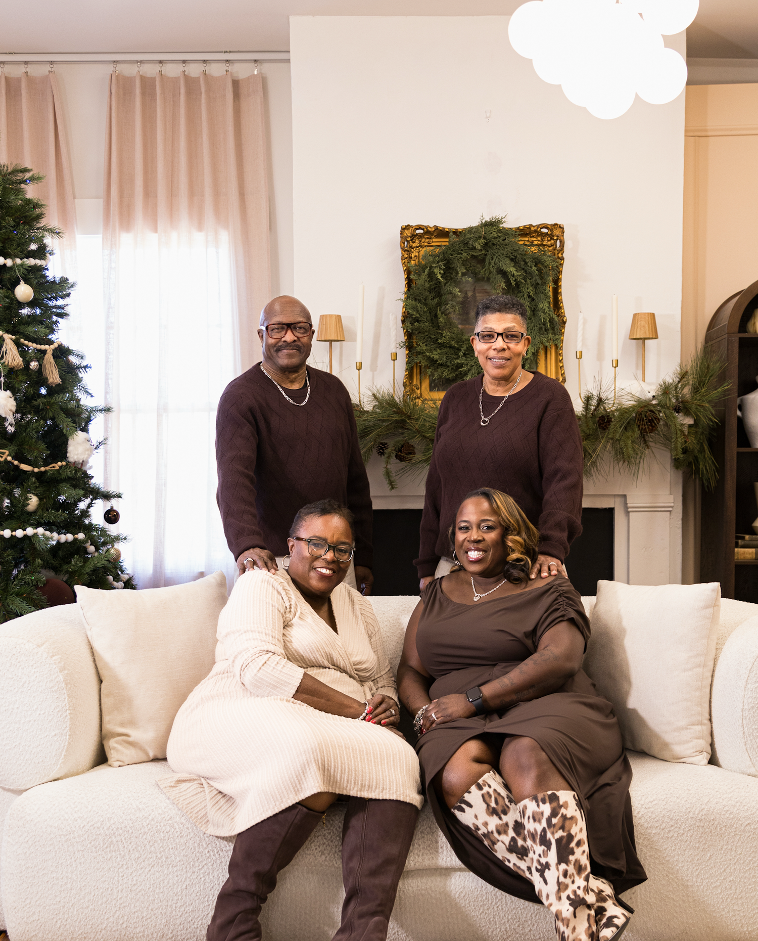 Family relaxes together on a white couch during holiday season with Christmas tree and garland decorations visible.