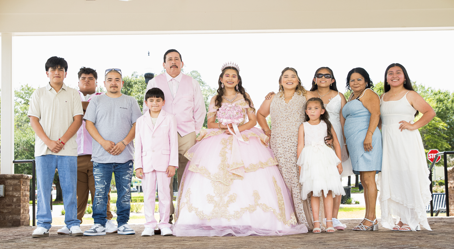 A row of children sitting together on a bench outdoors wearing white and light colored clothing.