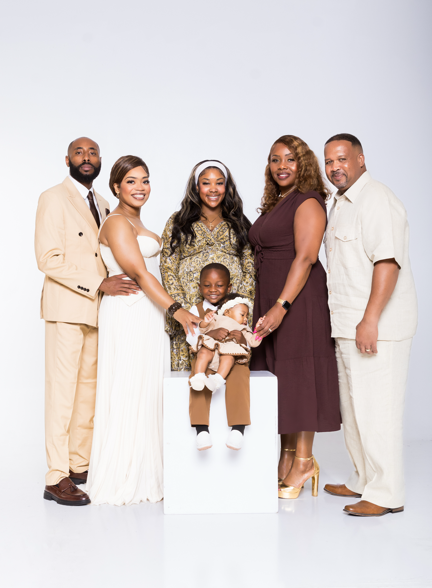 A joyful family portrait with six members dressed in cream and brown tones posing together on a white background.