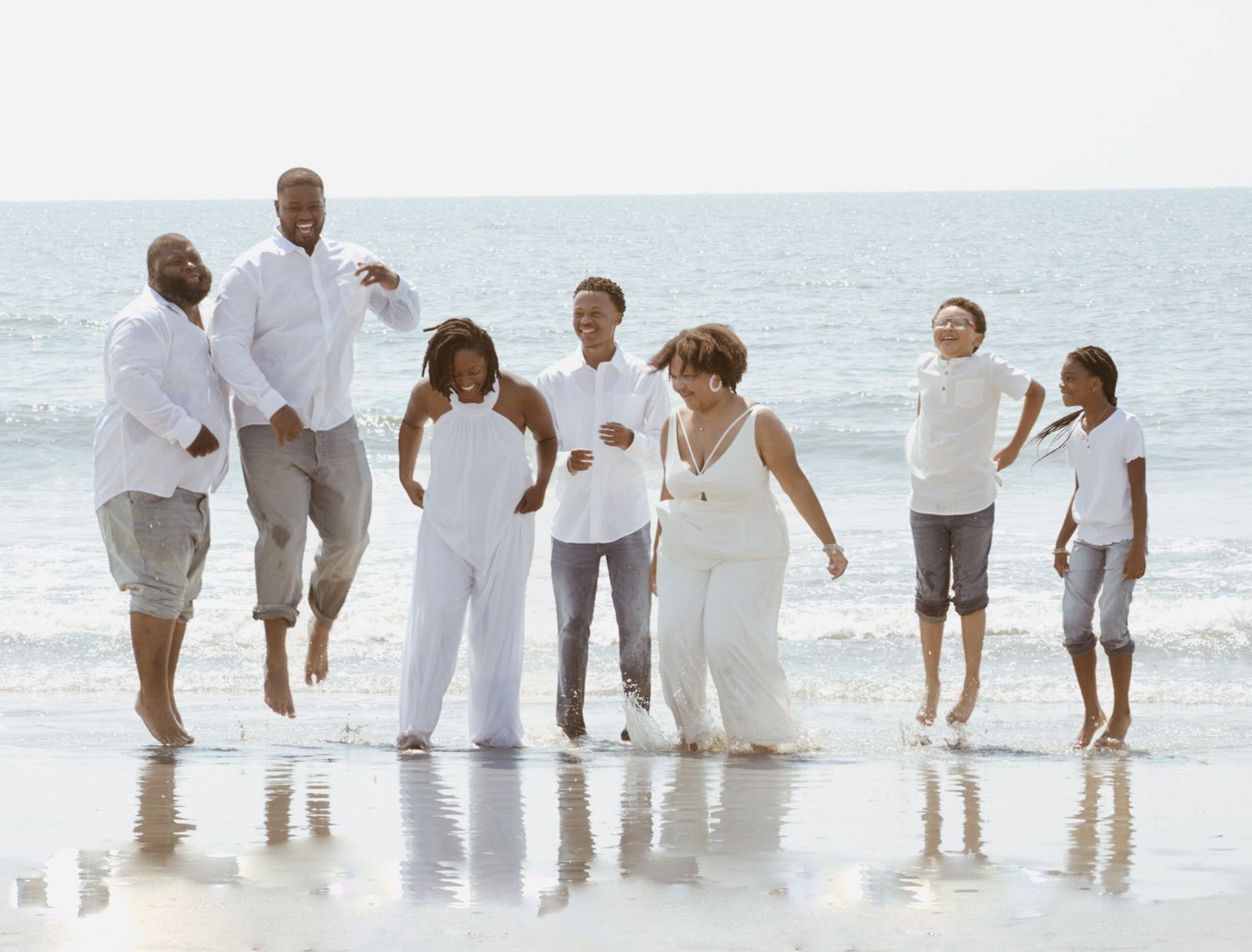 Family beach portrait featuring group in white outfits standing at the ocean's edge.