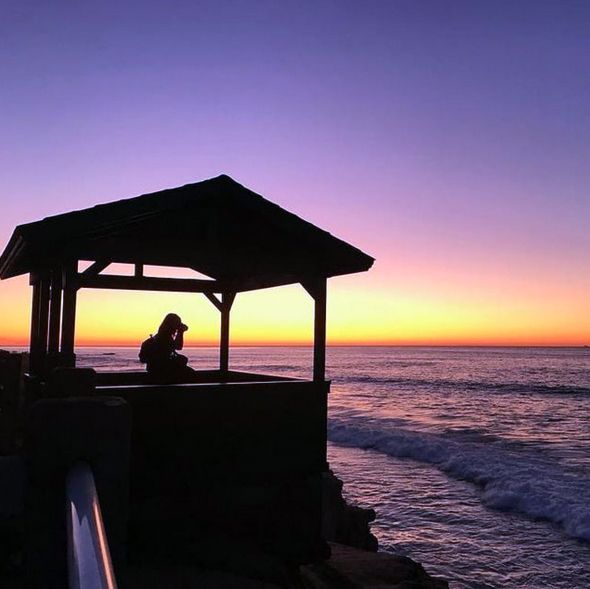 Silhouette of Joyce under a covered lookout watching sunset over the ocean.