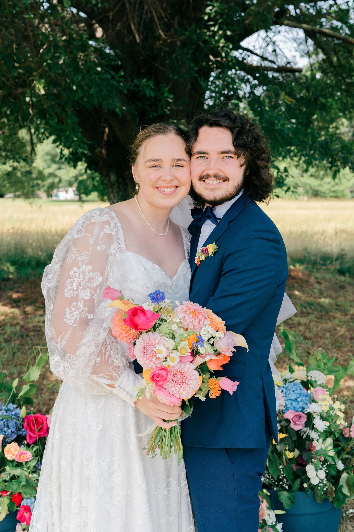 Wedding couple with vibrant floral bouquet posing in outdoor garden setting.