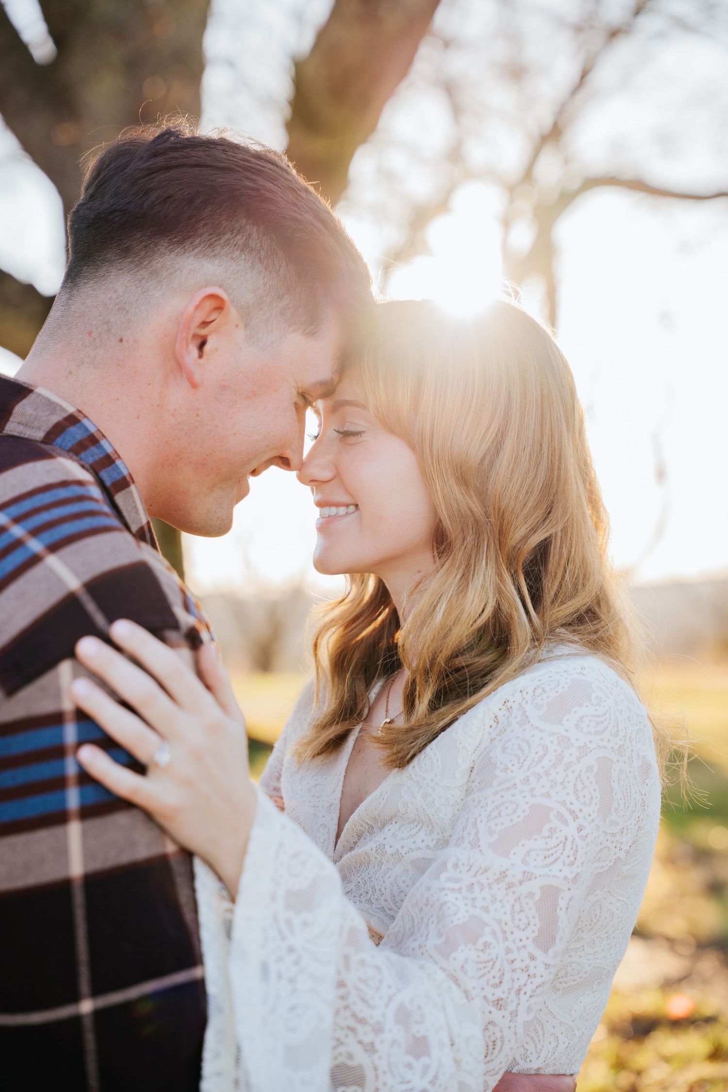 Romantic couple in autumn setting with woman in white lace dress embracing during golden hour.