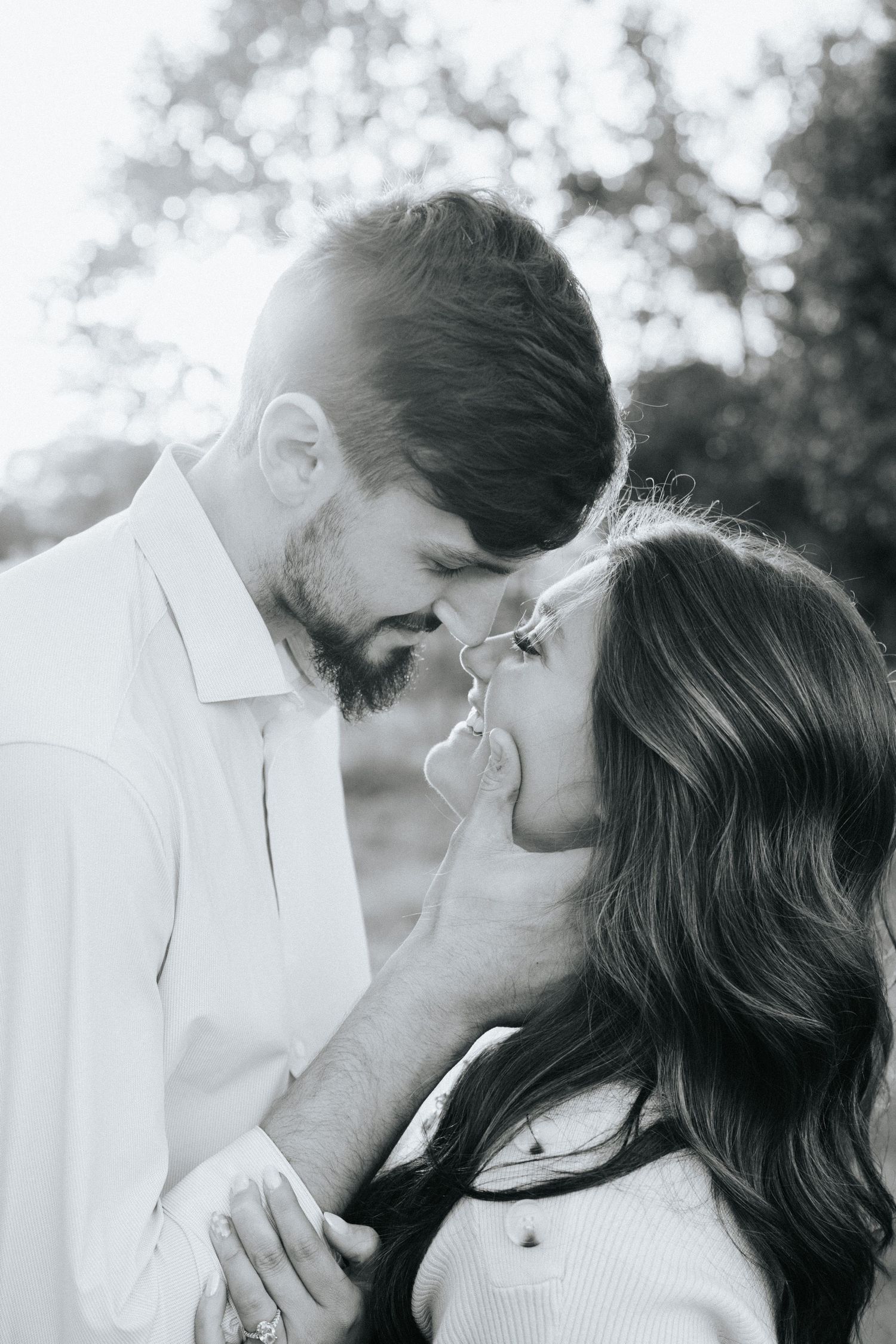 Romantic black and white portrait of a couple sharing an intimate moment outdoors in soft lighting.