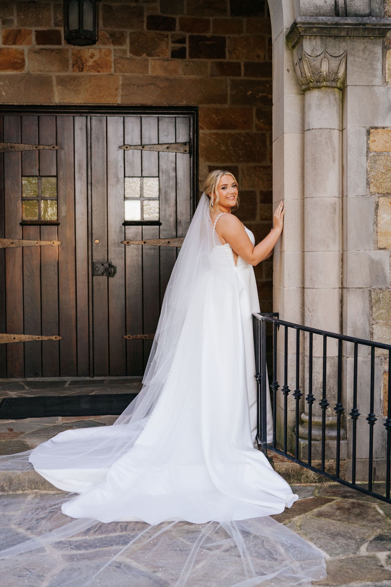 Elegant bridal train cascading across stone patio with rustic brick wall and black iron railings.