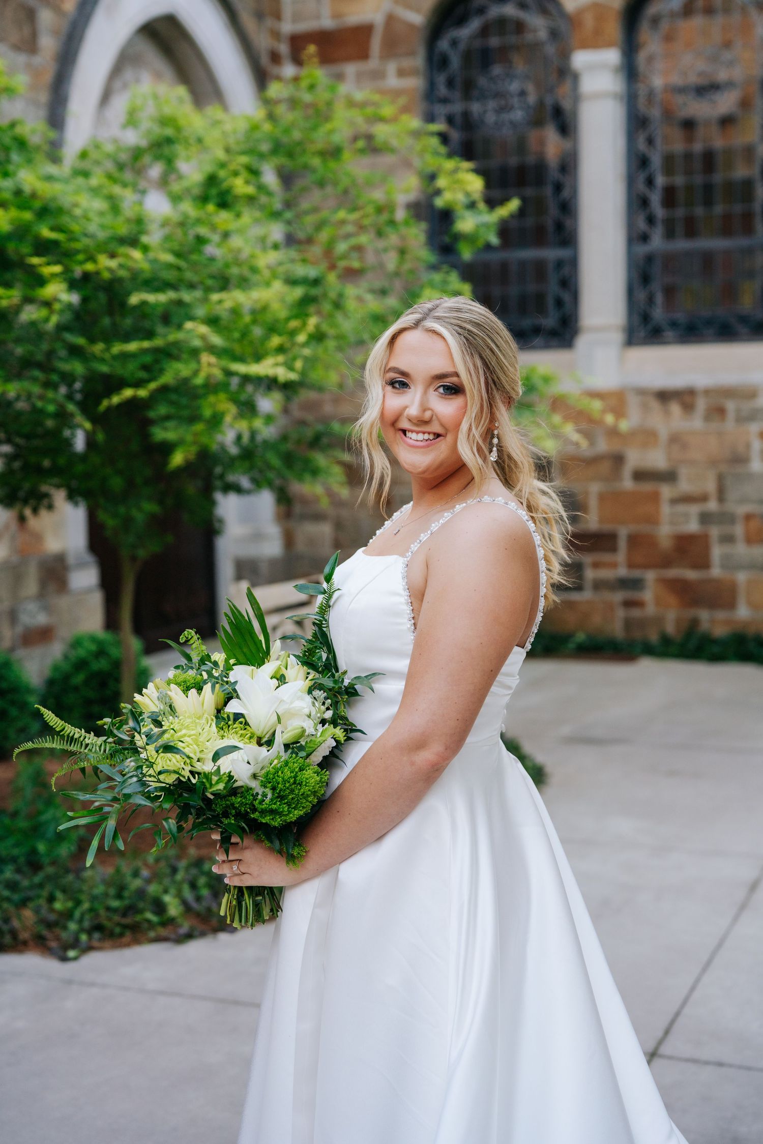Joyful bridal portrait showcasing a classic white wedding dress against stone church backdrop.