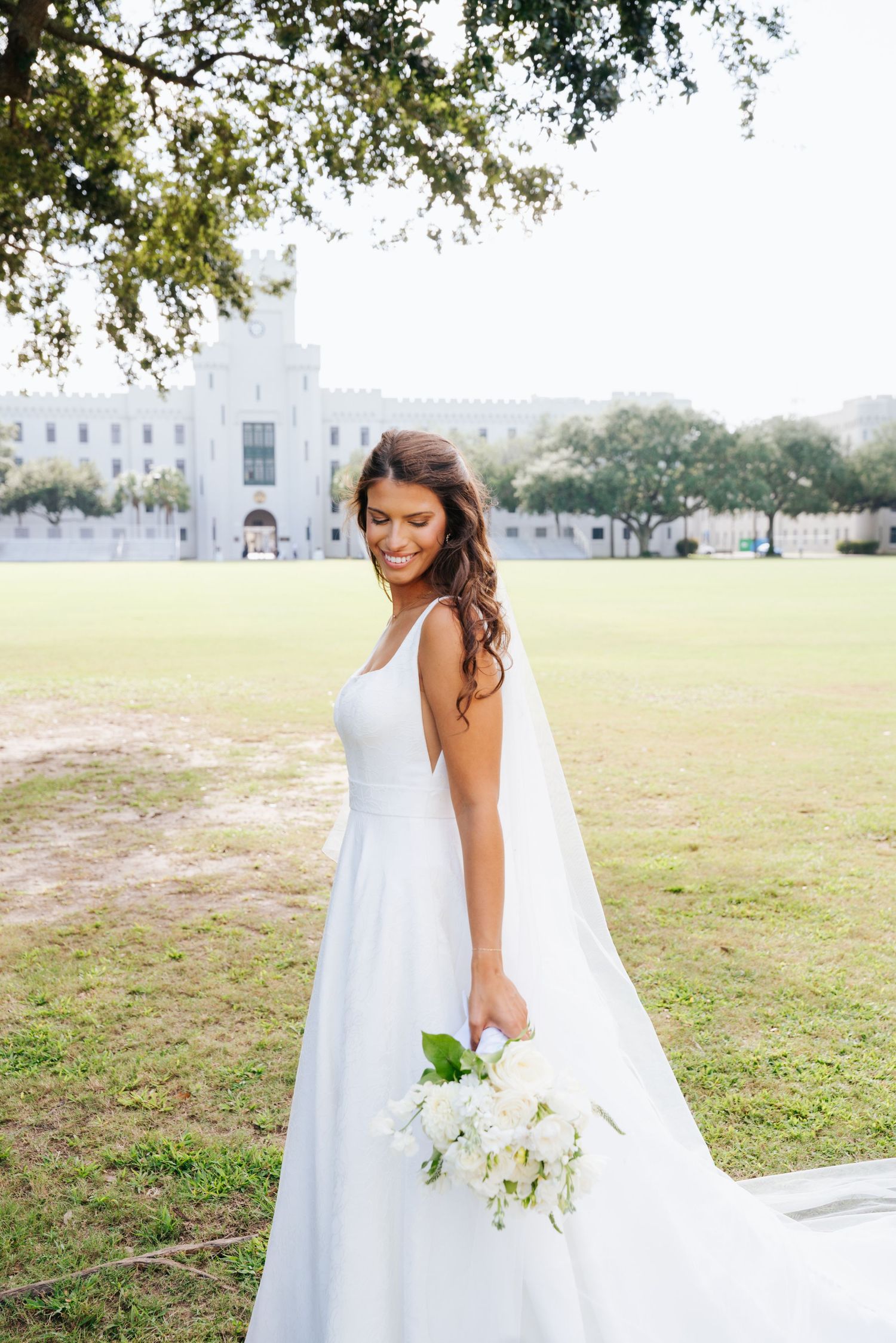 Elegant bridal portrait in a white gown with flowing veil on a grassy field in front of the Citadel.