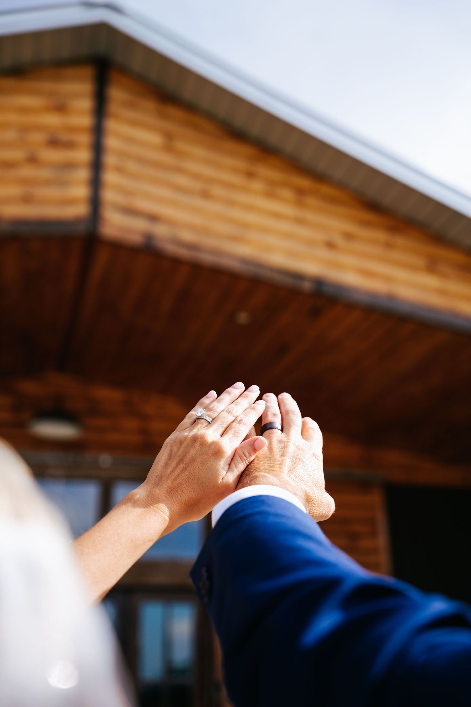 Hands raised in celebration against a wooden building exterior during a wedding celebration.