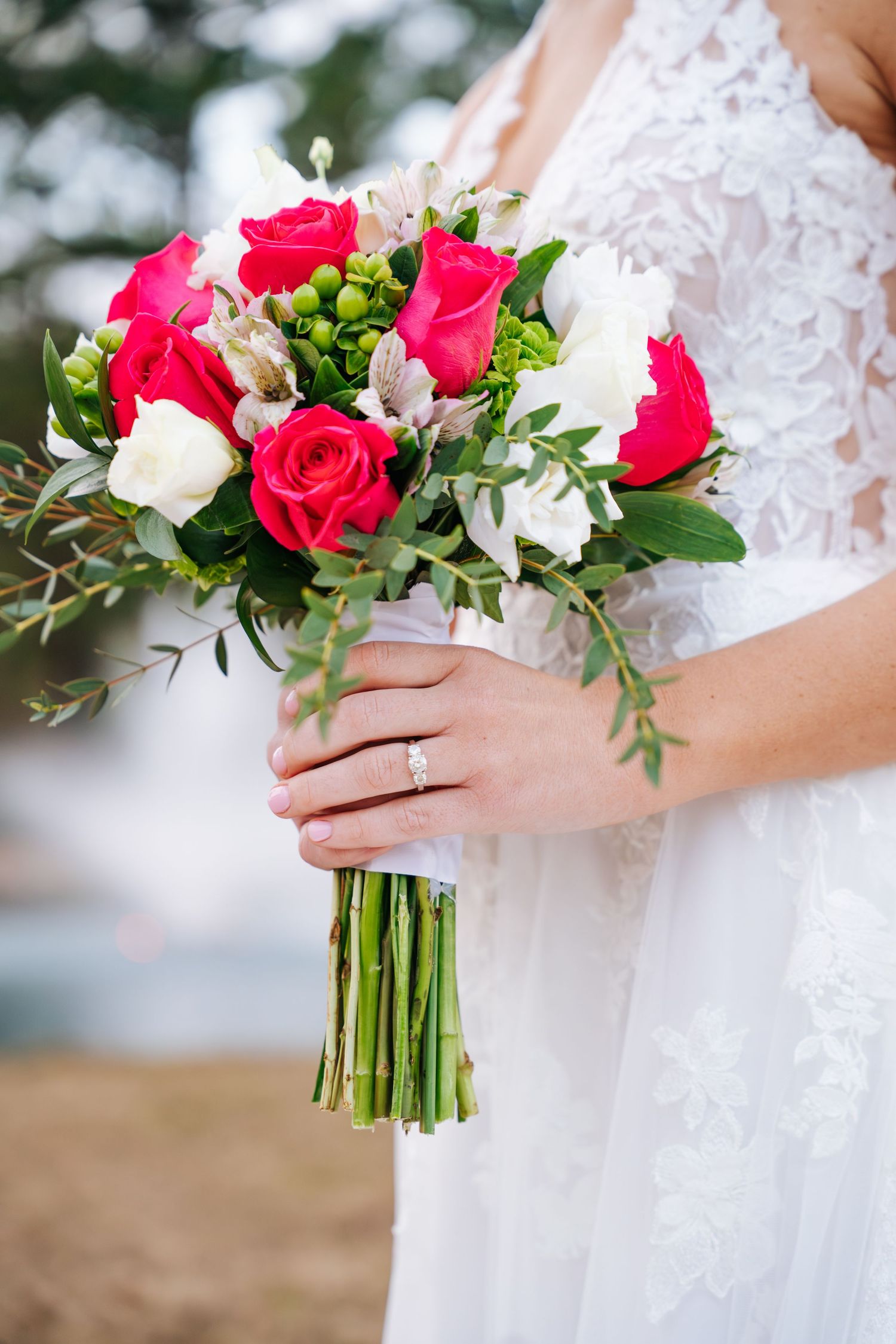 Close-up view of a bridal bouquet featuring pink roses, white flowers and green foliage against a white lace dress.