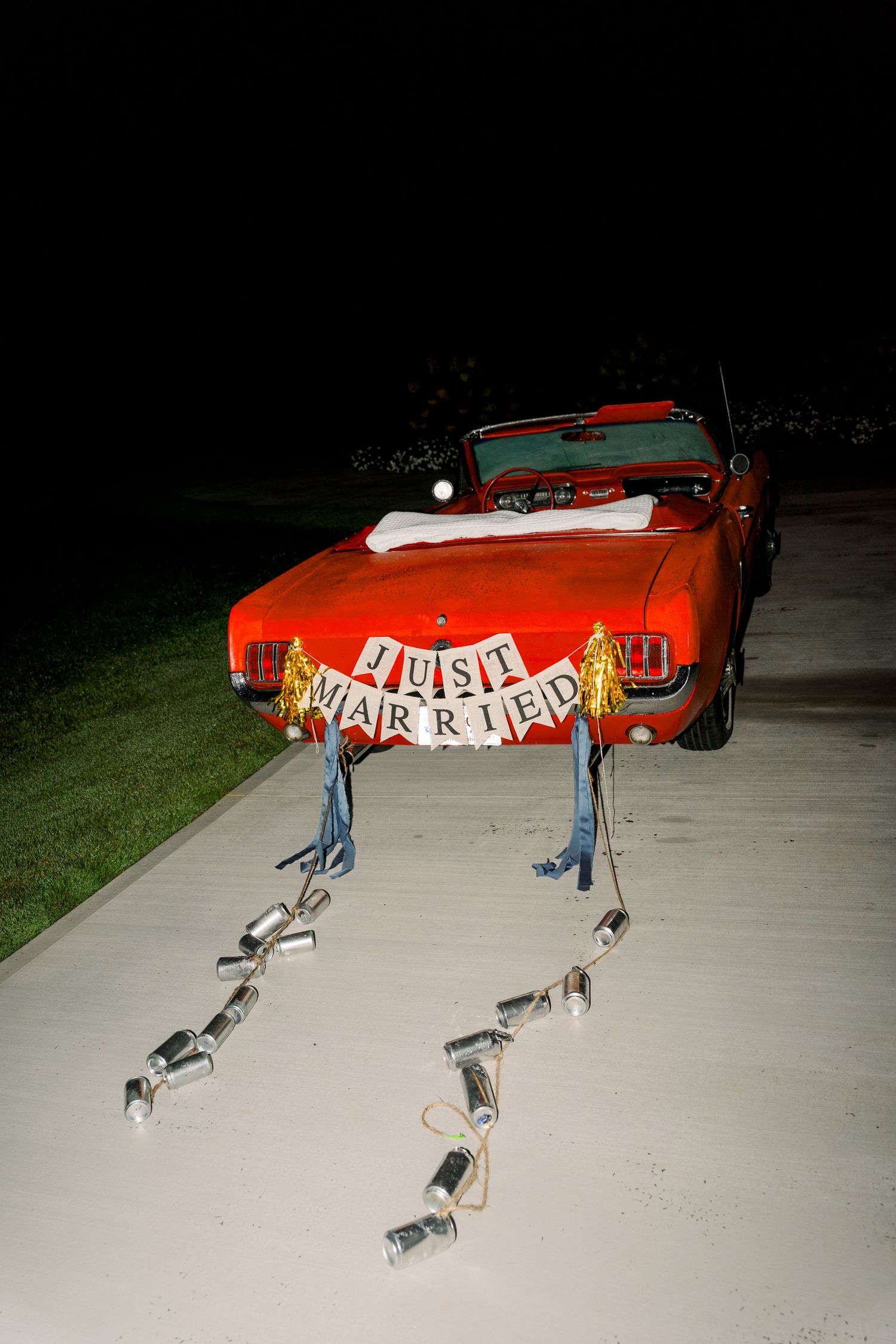Red convertible car decorated with Just Married sign and tin cans on driveway at night.