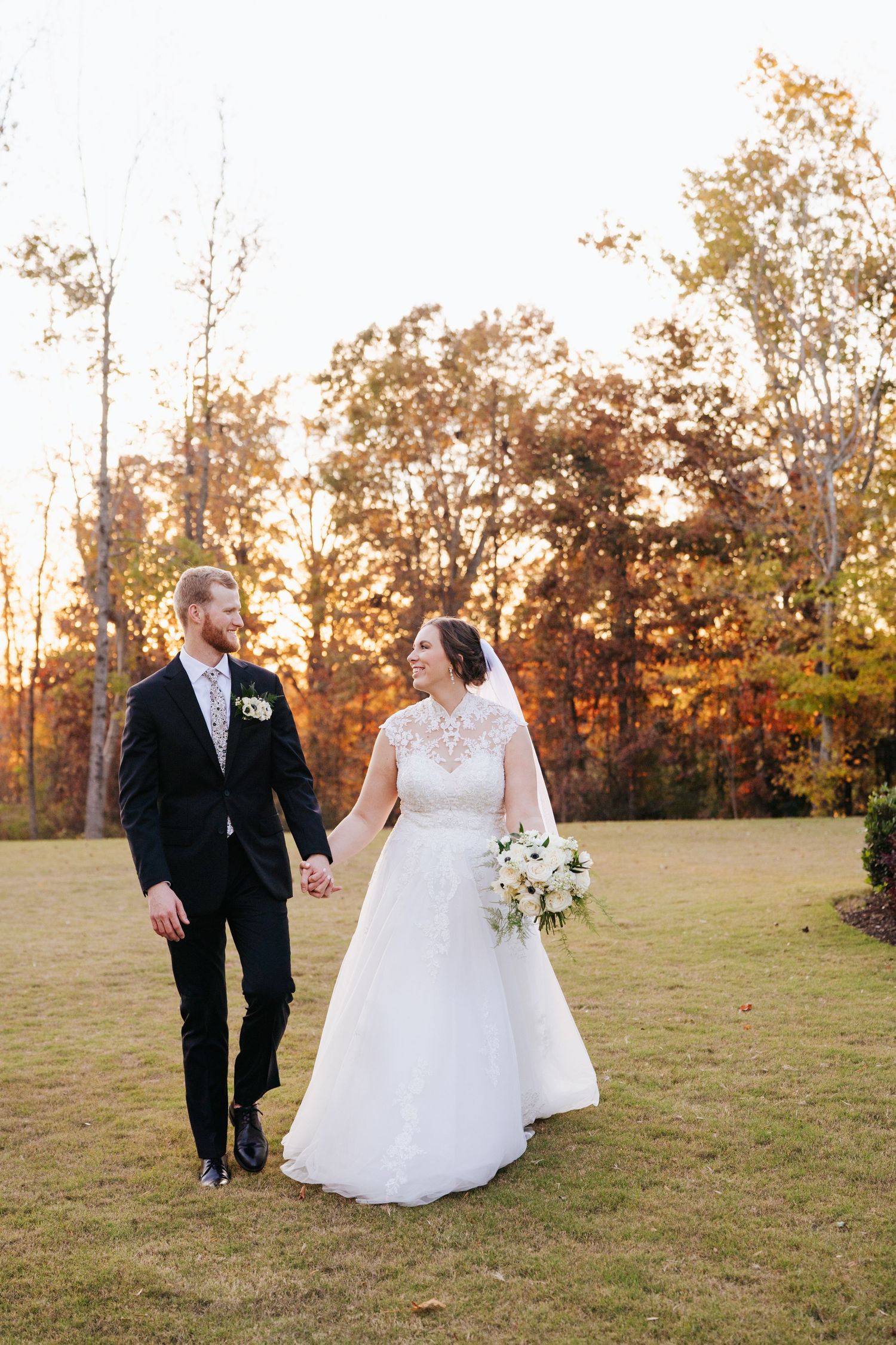 A romantic sunset wedding photoshoot with a couple walking together in a grassy field.