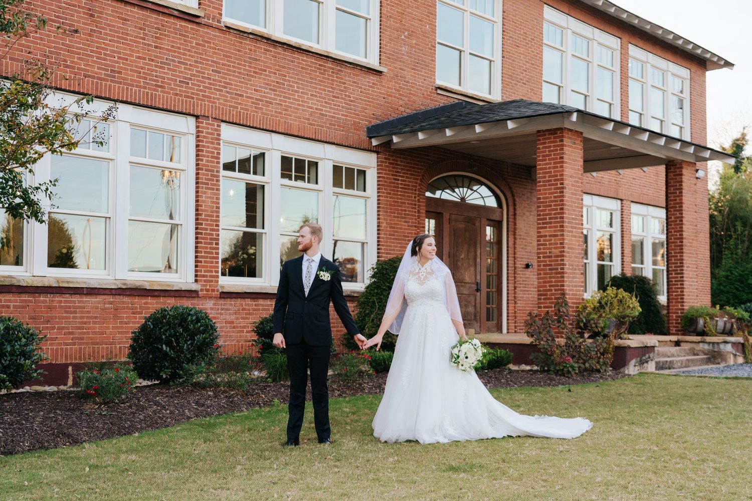 Wedding party arranged in front of traditional red brick building exterior.