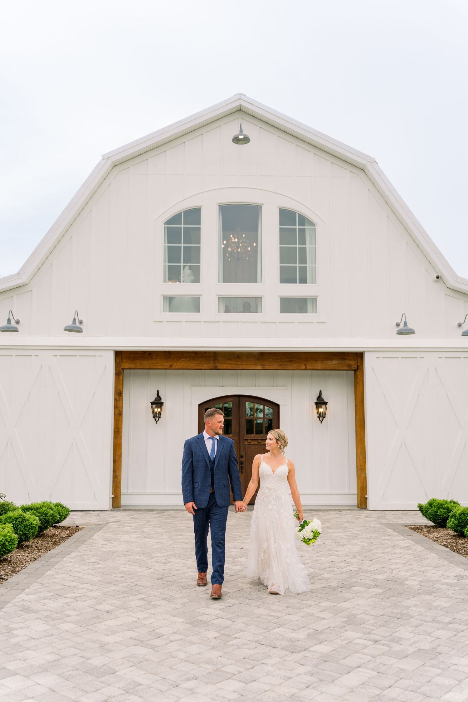 Bride and groom holding hands walking in front of a white barn wedding venue on their special day.