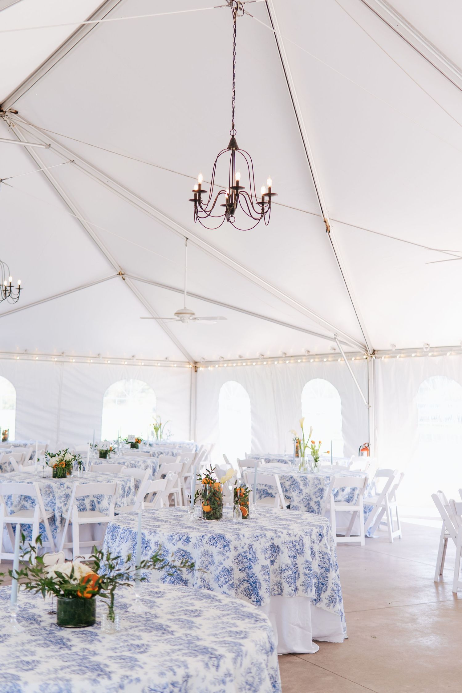 White wedding reception tent decorated with blue and white linens and elegant chandeliers.