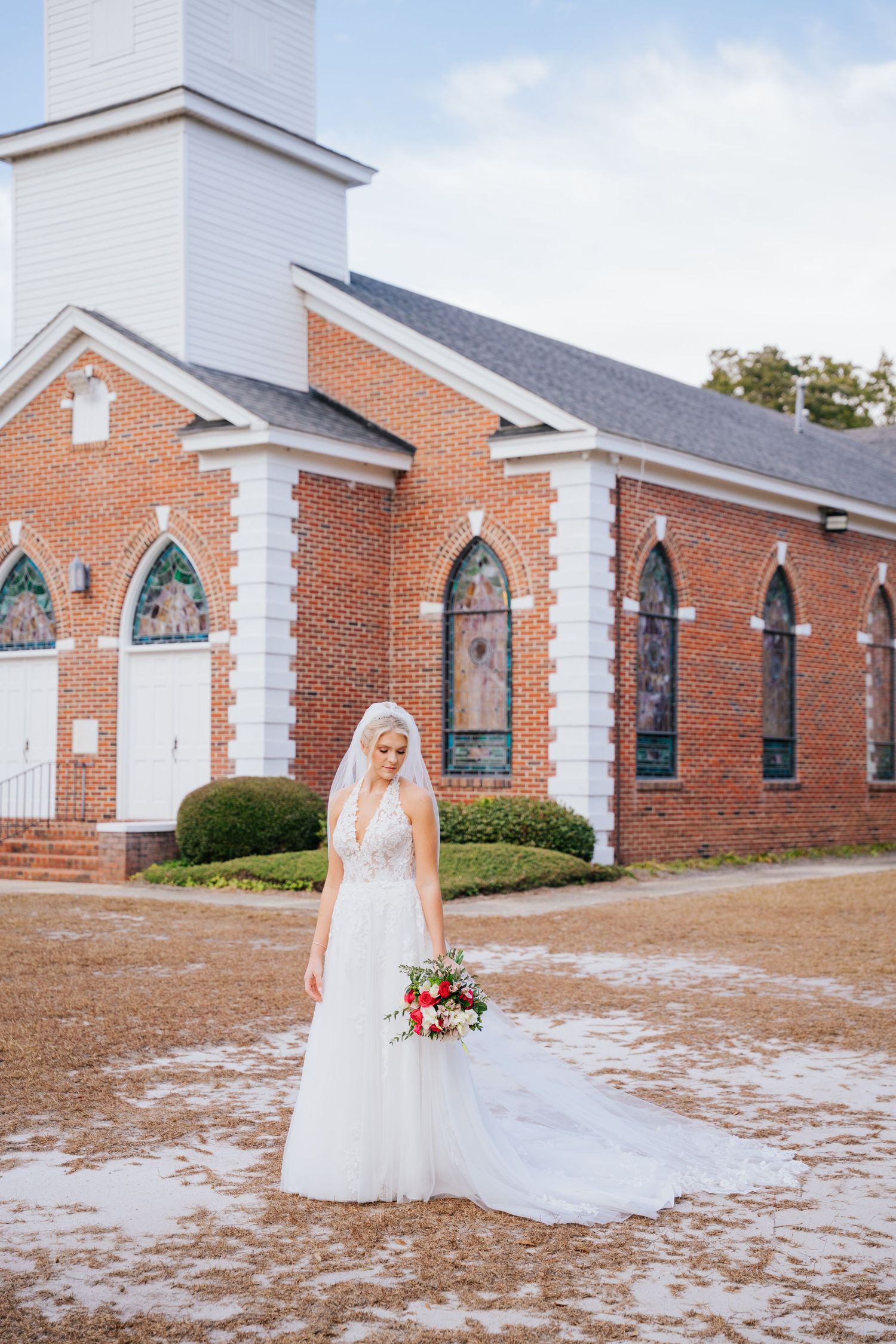 A beautiful brick church with arched stained glass windows and white trim serves as backdrop for a winter wedding photo.