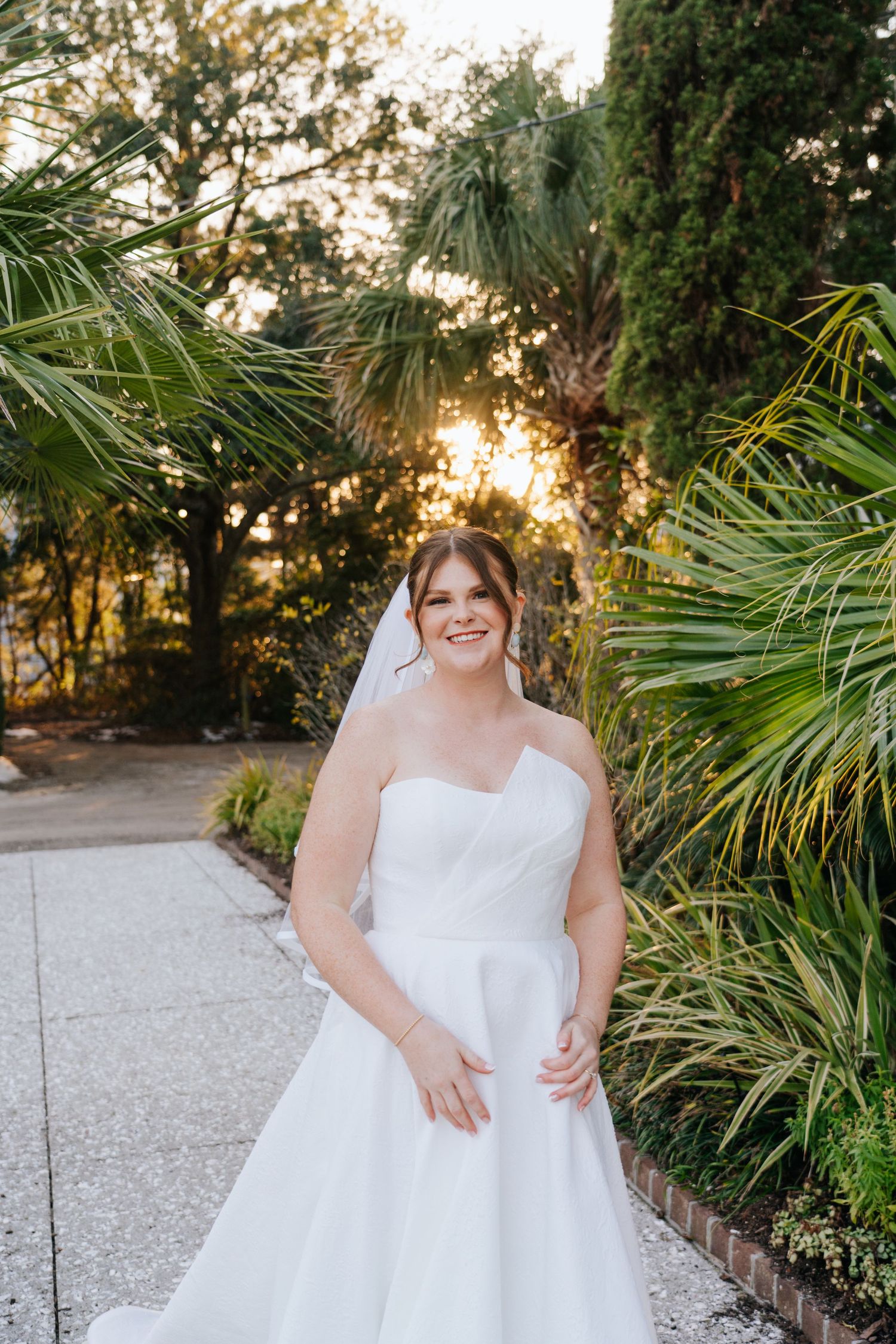 A white wedding dress is photographed in a garden setting during golden hour.