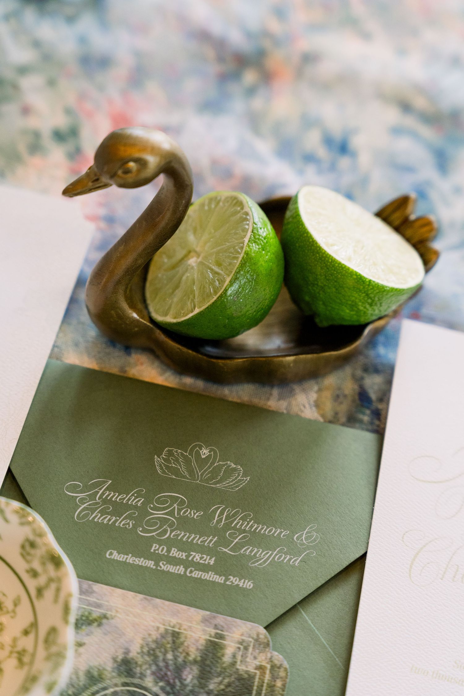 Elegant wedding invitation suite in sage green with a brass swan dish holding fresh lime halves, addressed to Amelia Rose Whitmore.