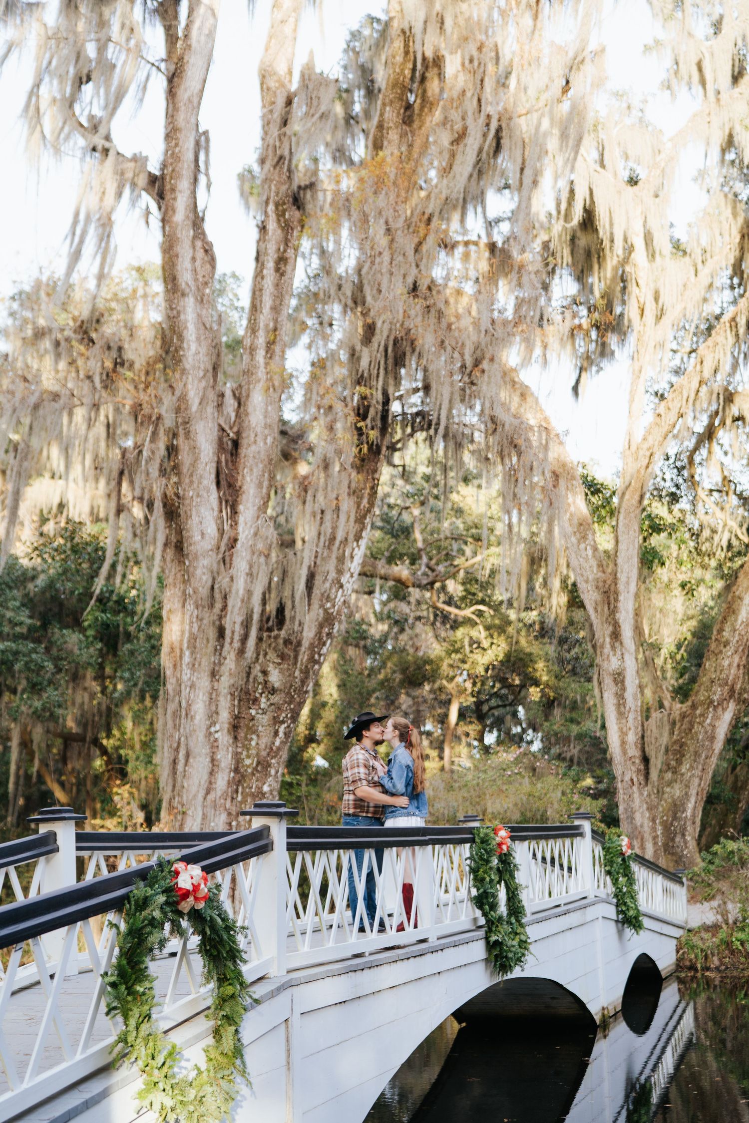 Couple sharing a romantic moment on a decorated bridge with Spanish moss hanging overhead.