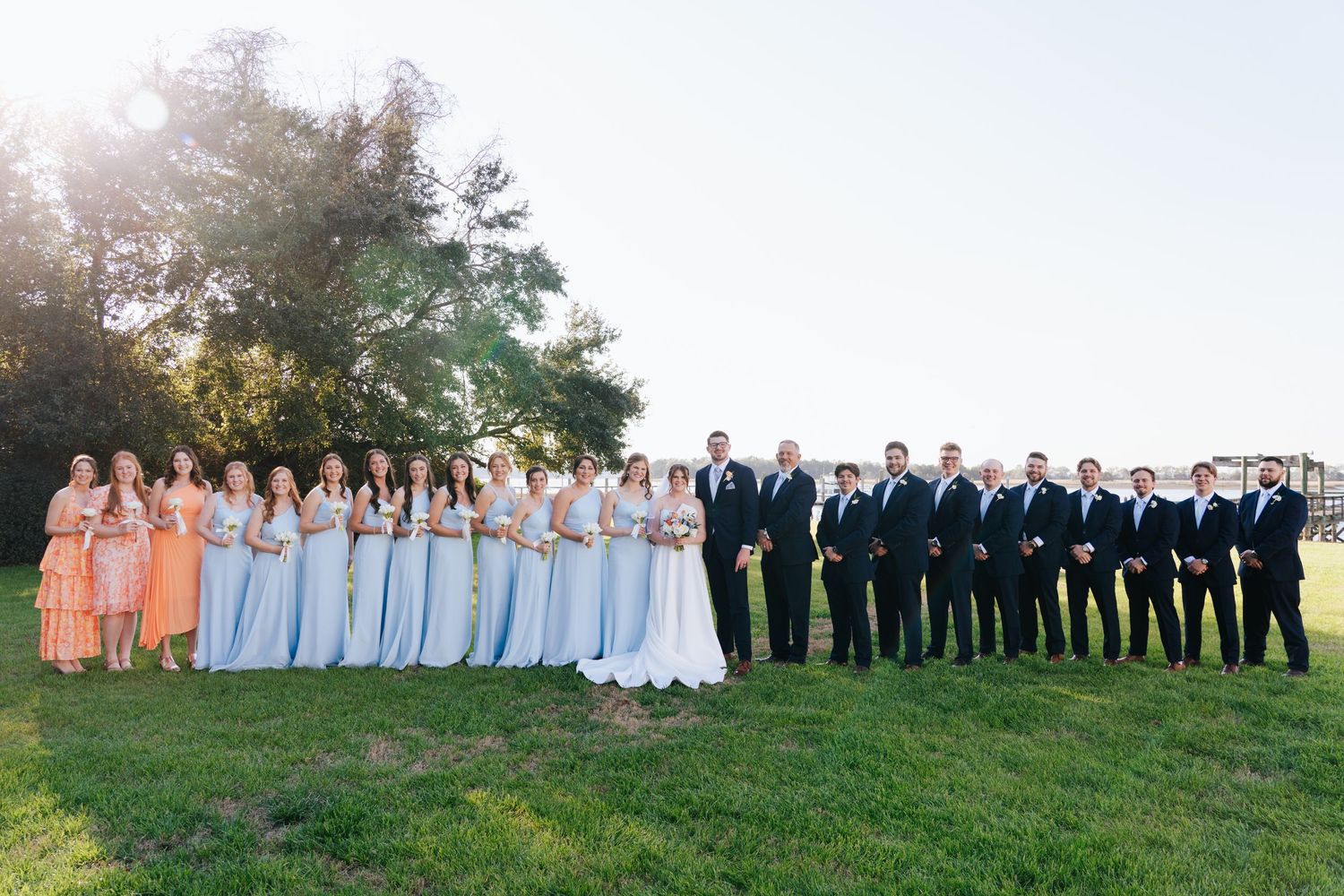 Wedding party members lined up outdoors for formal group photos at sunset.