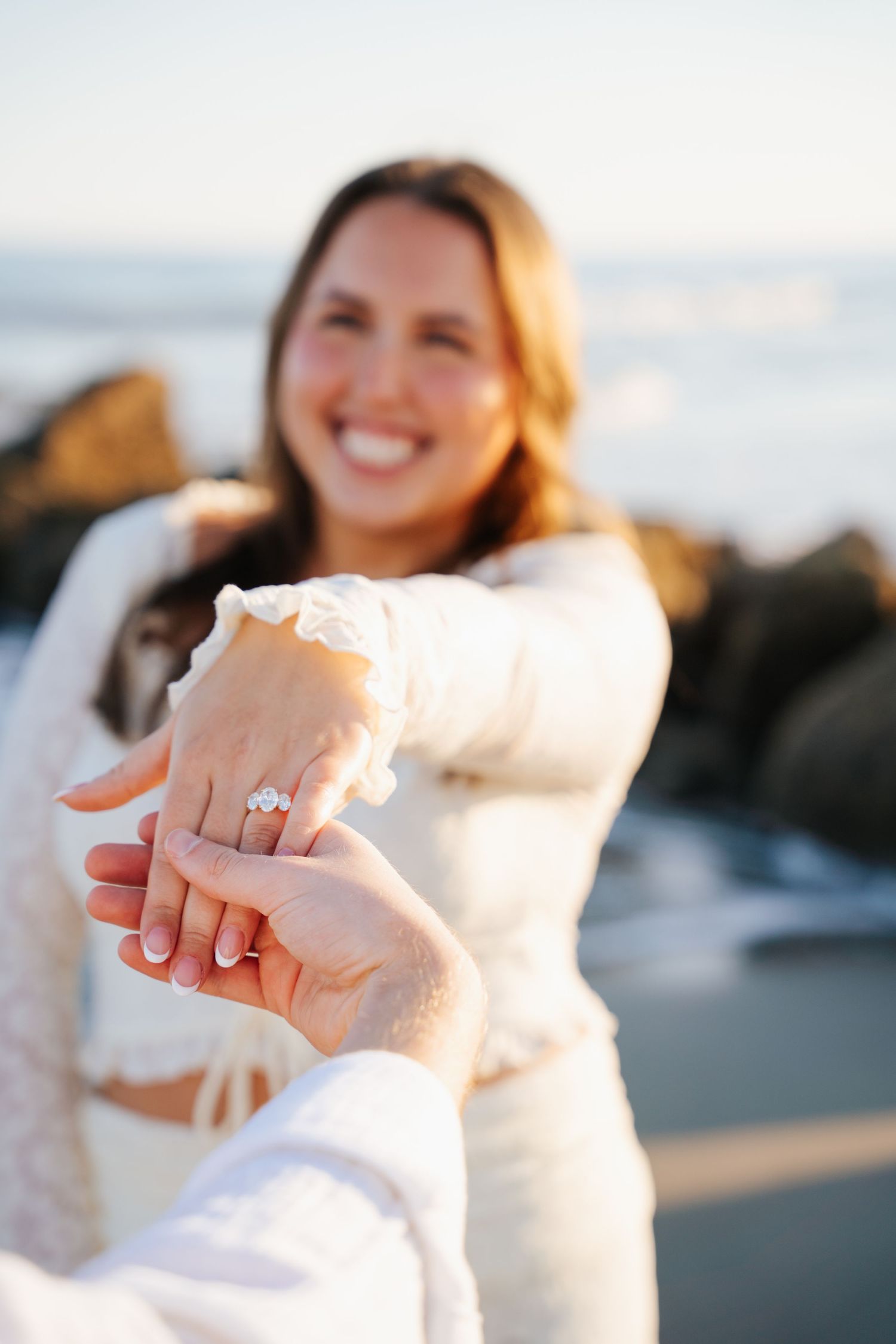 A series of engagement photos showing close-up shots of a sparkling diamond ring on a beach at sunset.
