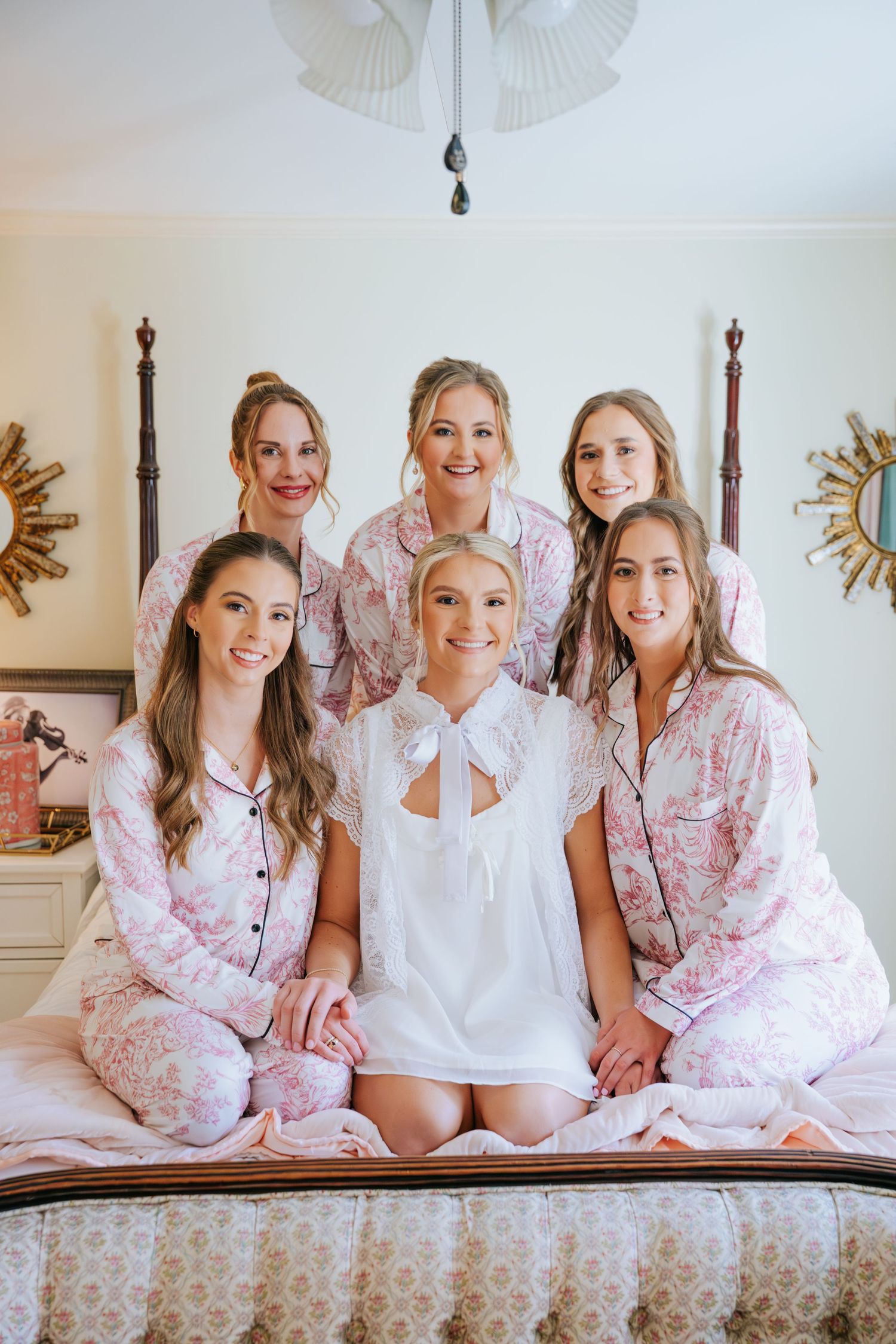 A group wearing matching pink and white pajamas poses together on a bed during a sleepover or special occasion.