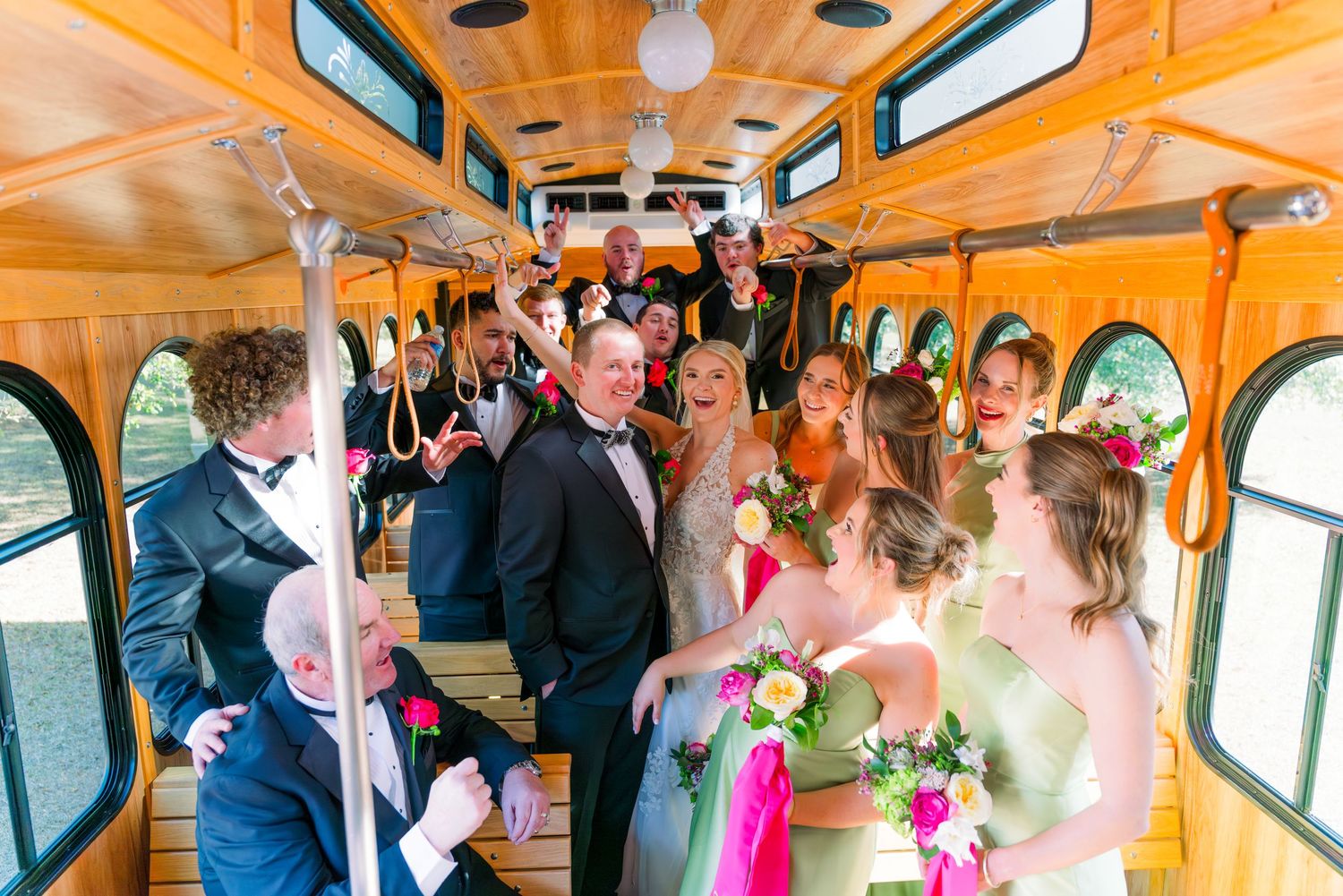 Wedding party celebrating inside a decorated trolley bus, with bridesmaids in green dresses and groomsmen in tuxedos.