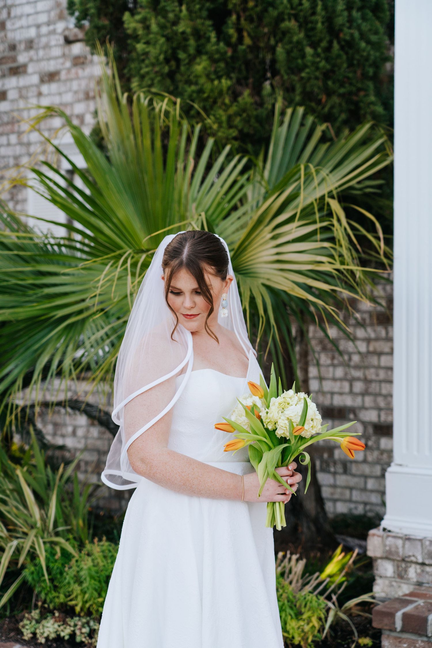 A wedding dress and veil are captured near tropical foliage and white columns.