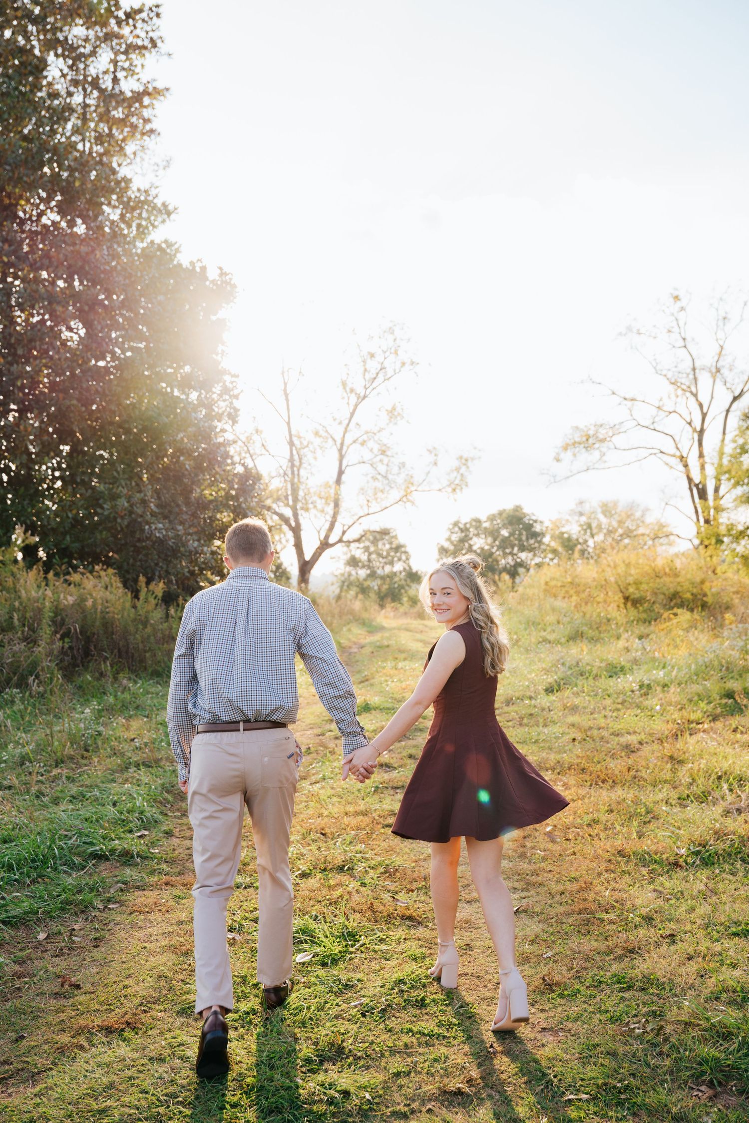 Two people walk hand in hand up a grassy hillside during golden hour sunset, creating a romantic silhouette.
