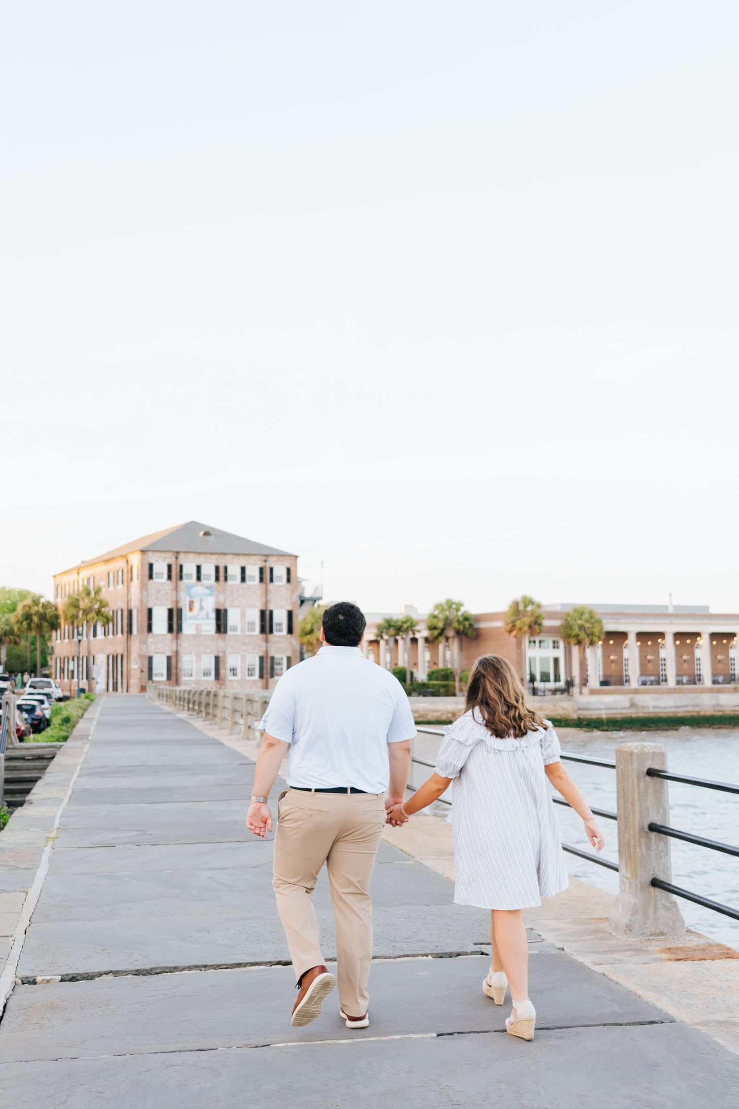 Couple walks hand in hand along Charleston's waterfront pier at sunset.