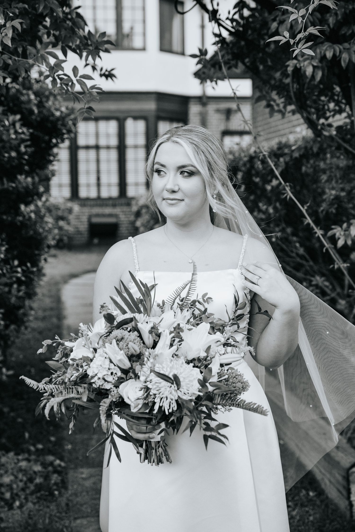 A bride in a white wedding dress holds a lush bouquet of flowers in front of a historic building.