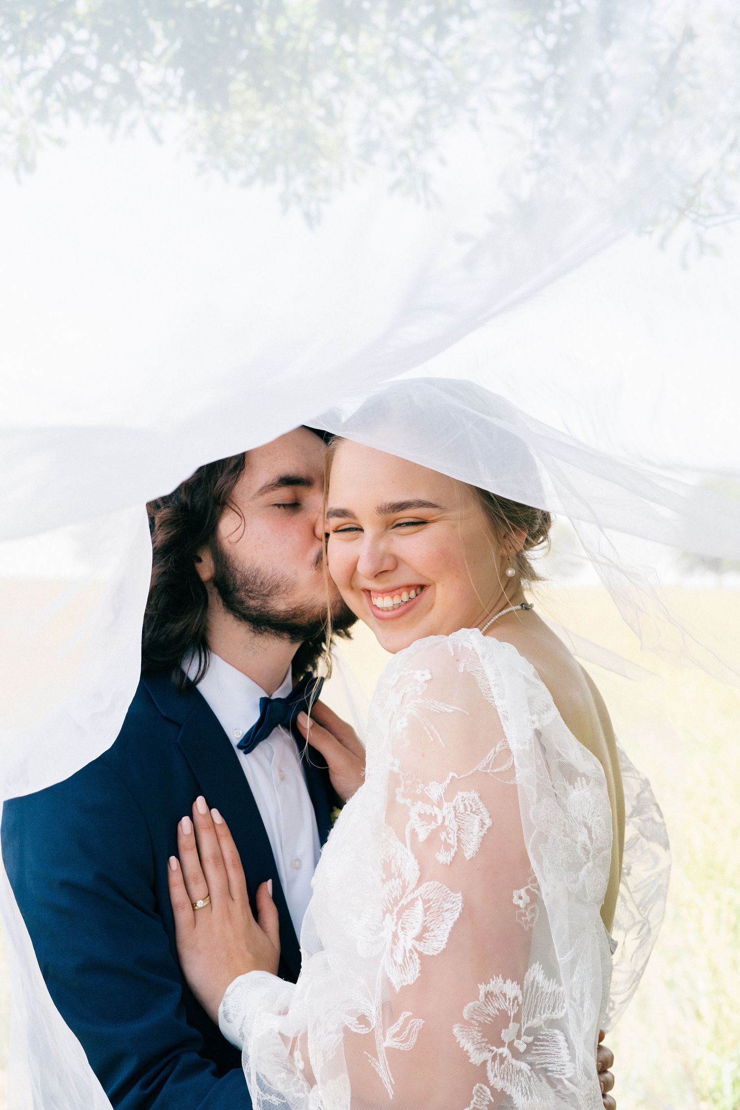 An intimate wedding portrait showing tender moments between a couple in white lace and navy attire.