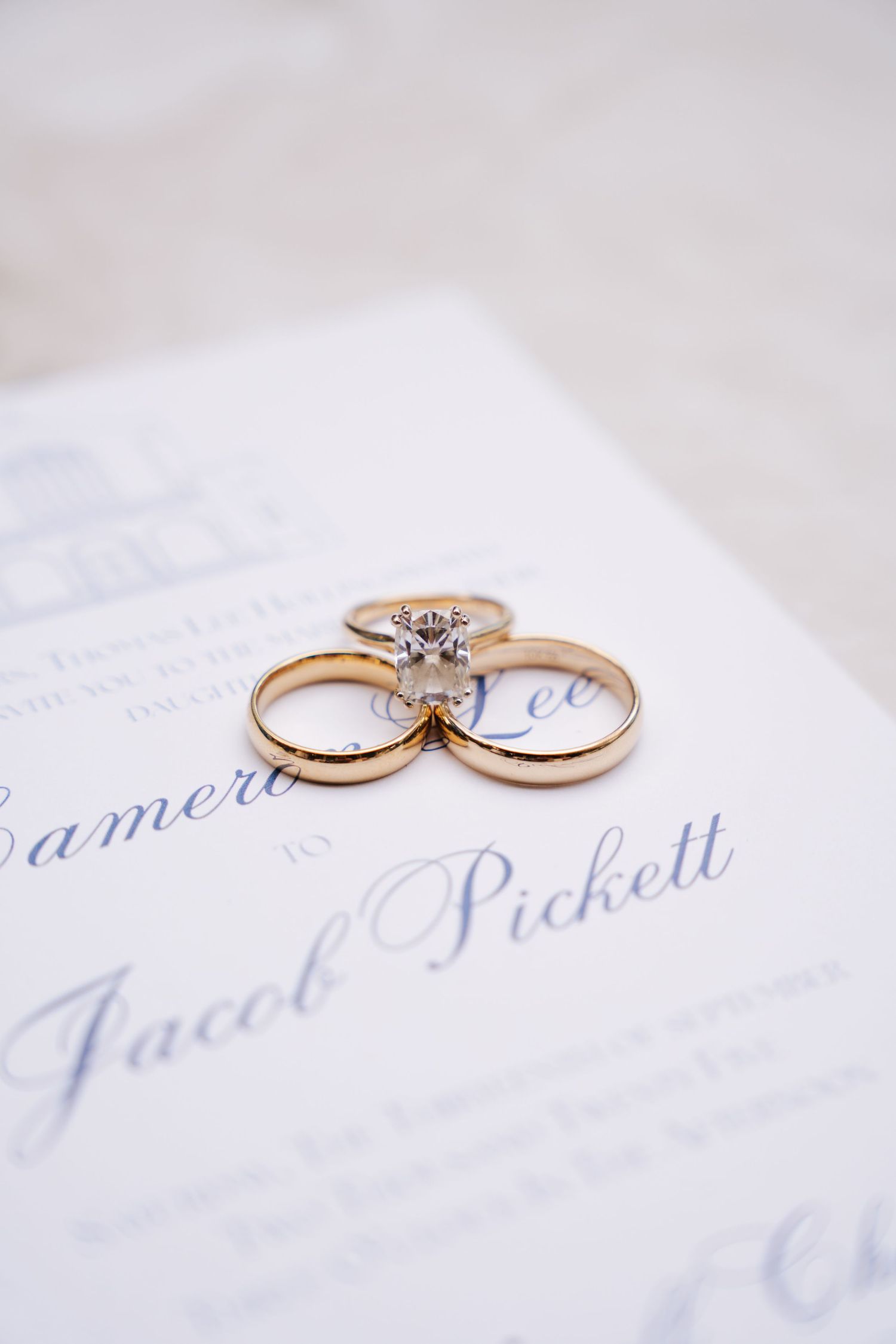 Three gold wedding rings arranged on elegant blue calligraphy wedding stationery.
