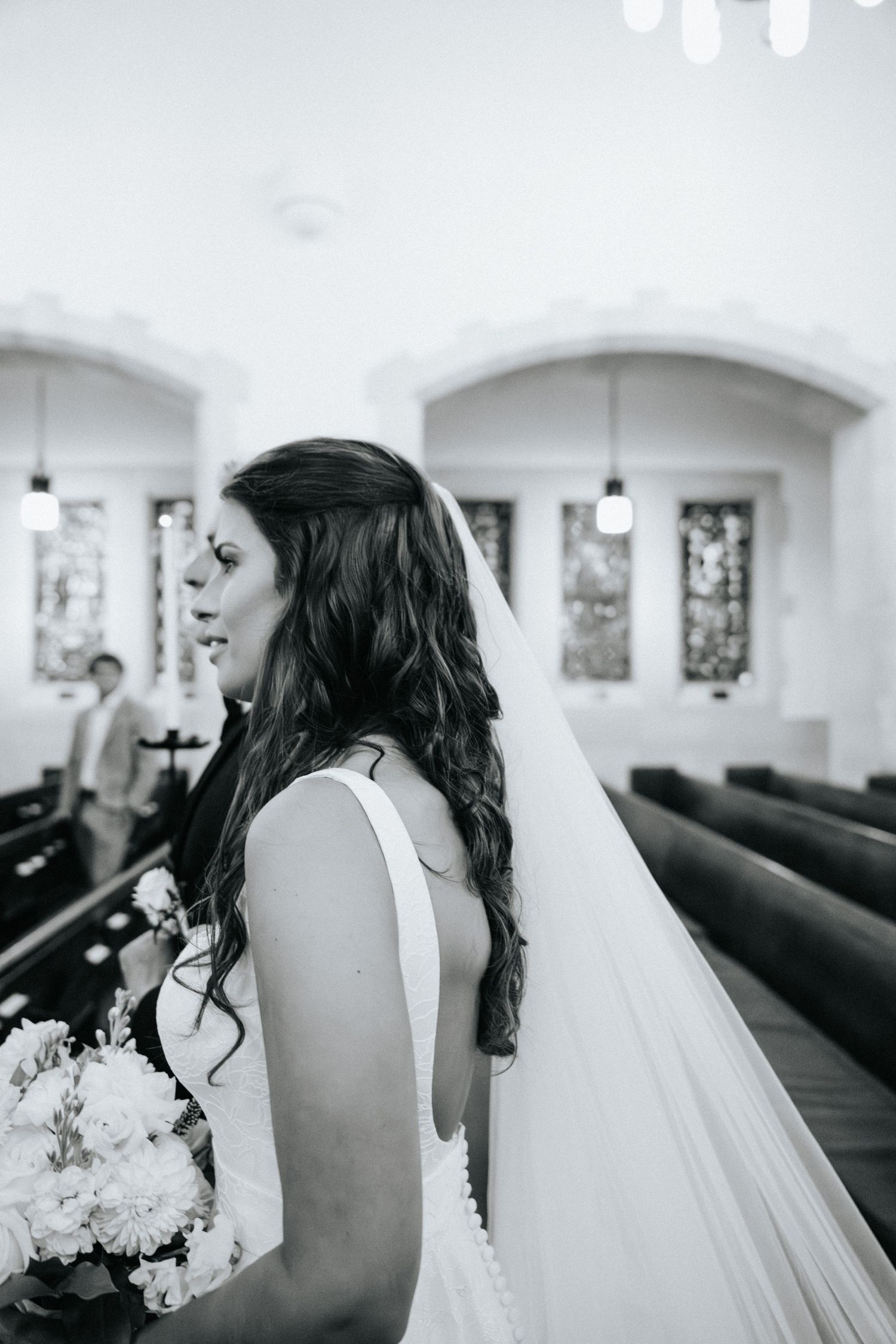 Black and white photo showing the side detail of a wedding dress in a church setting.