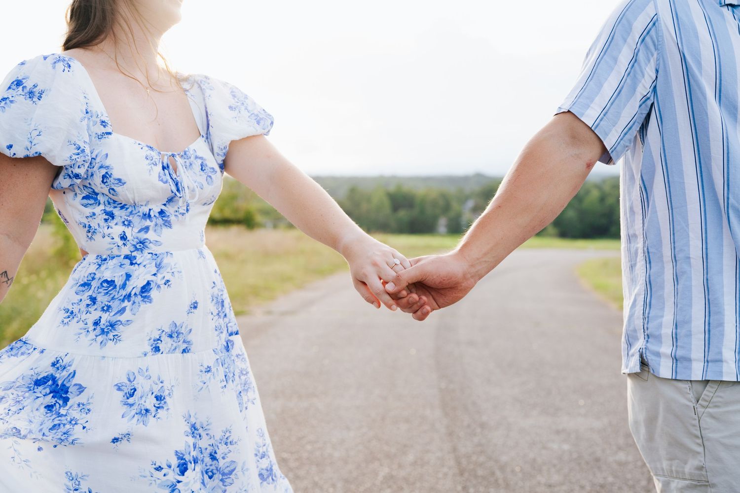 A couple holding hands on a country road, with a blue floral dress and striped shirt visible.