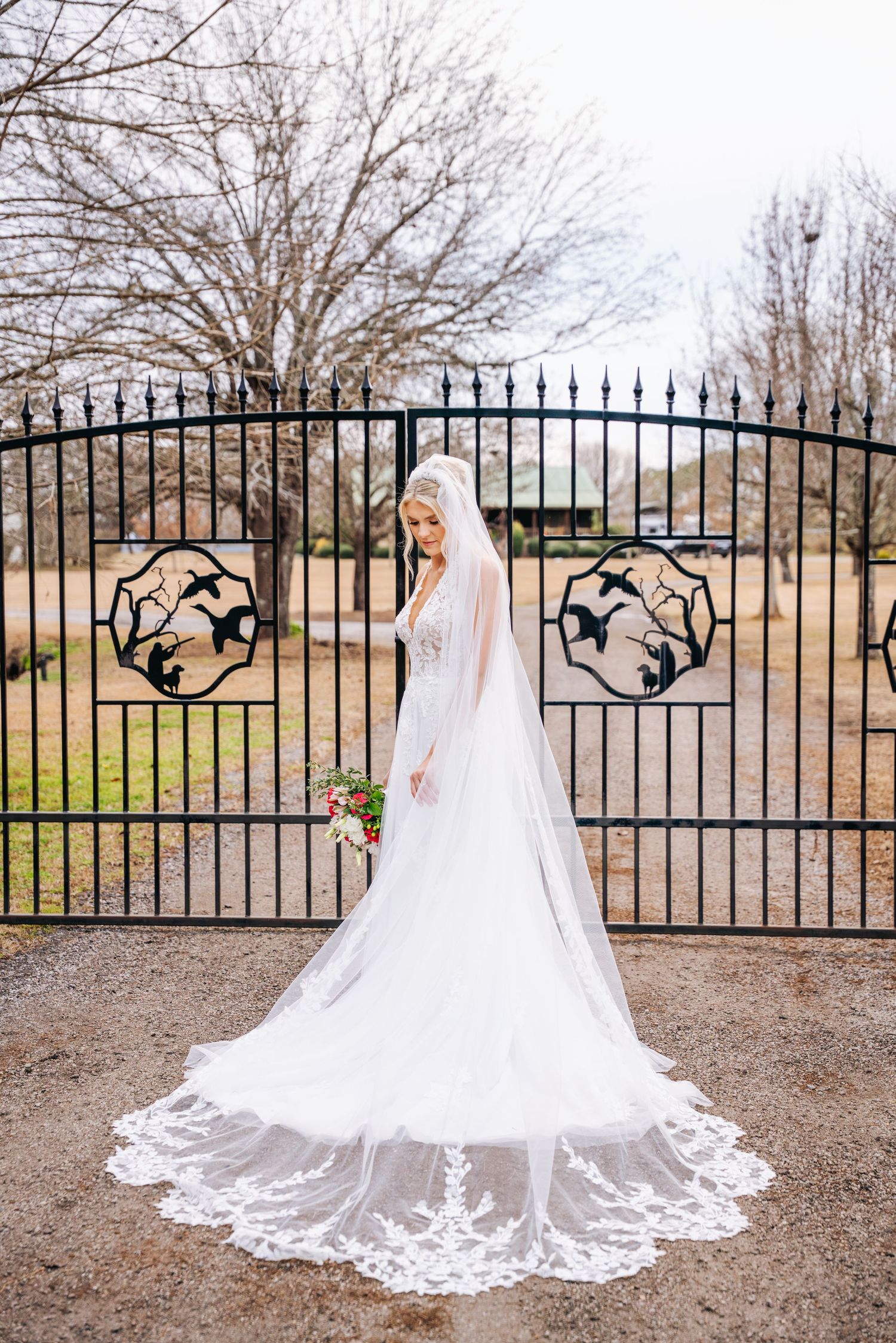 A cathedral-length lace veil with intricate embroidery details spreads elegantly across the ground near an ornate iron gate.