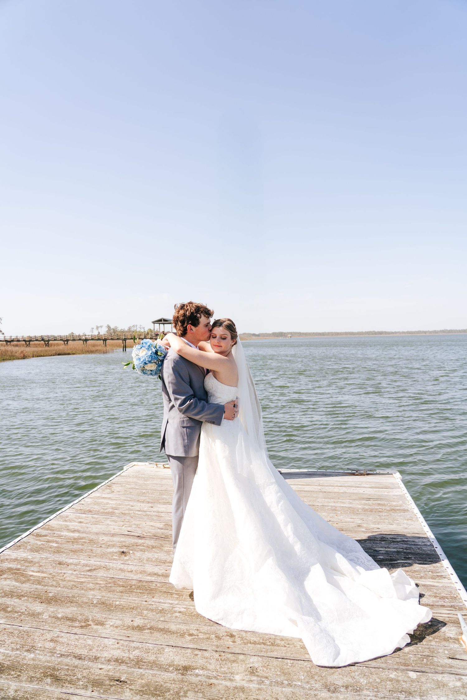 Newlyweds embracing on a wooden dock overlooking a serene lake.