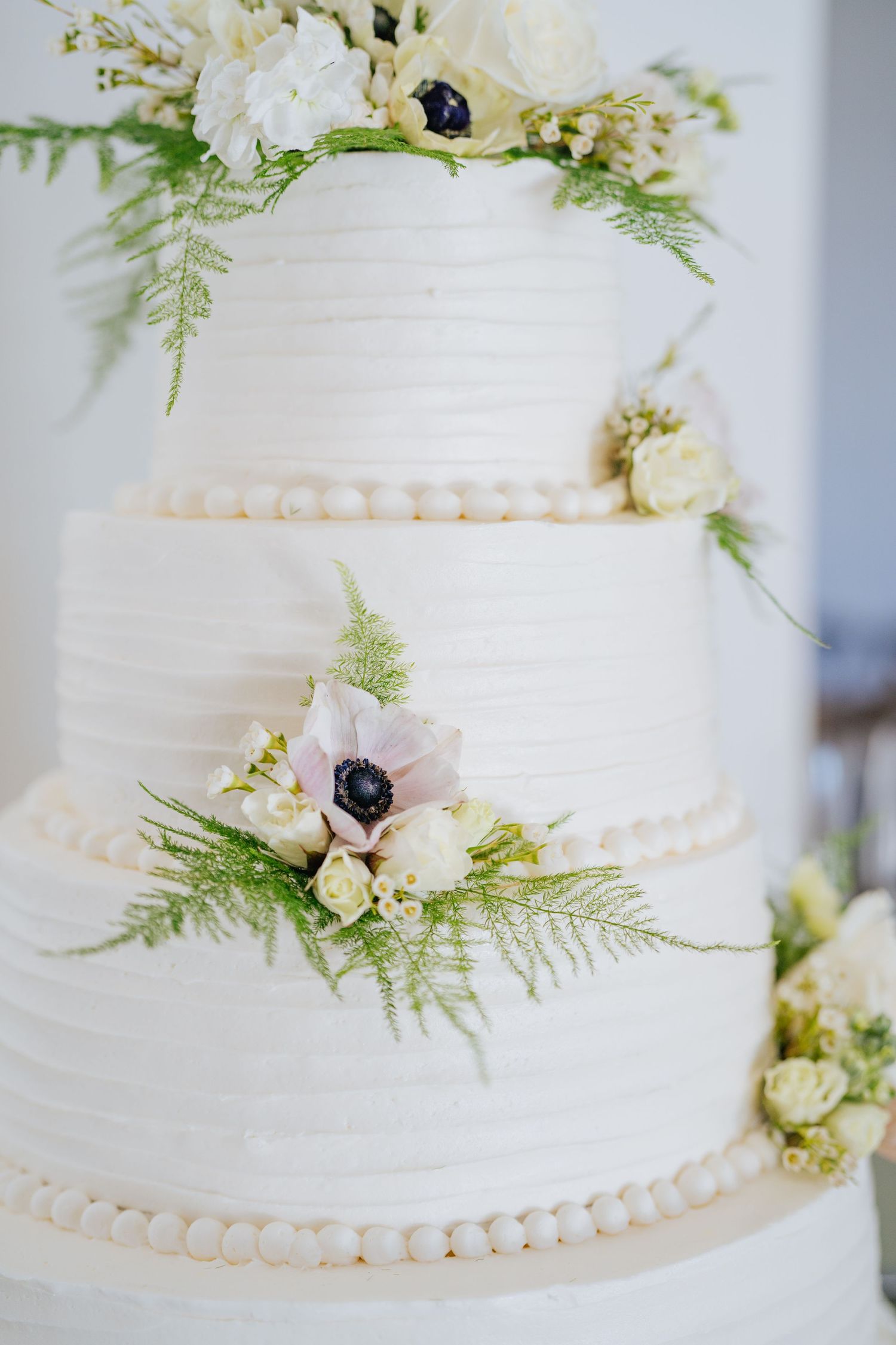 White tiered wedding cake decorated with delicate ferns and small floral accents.