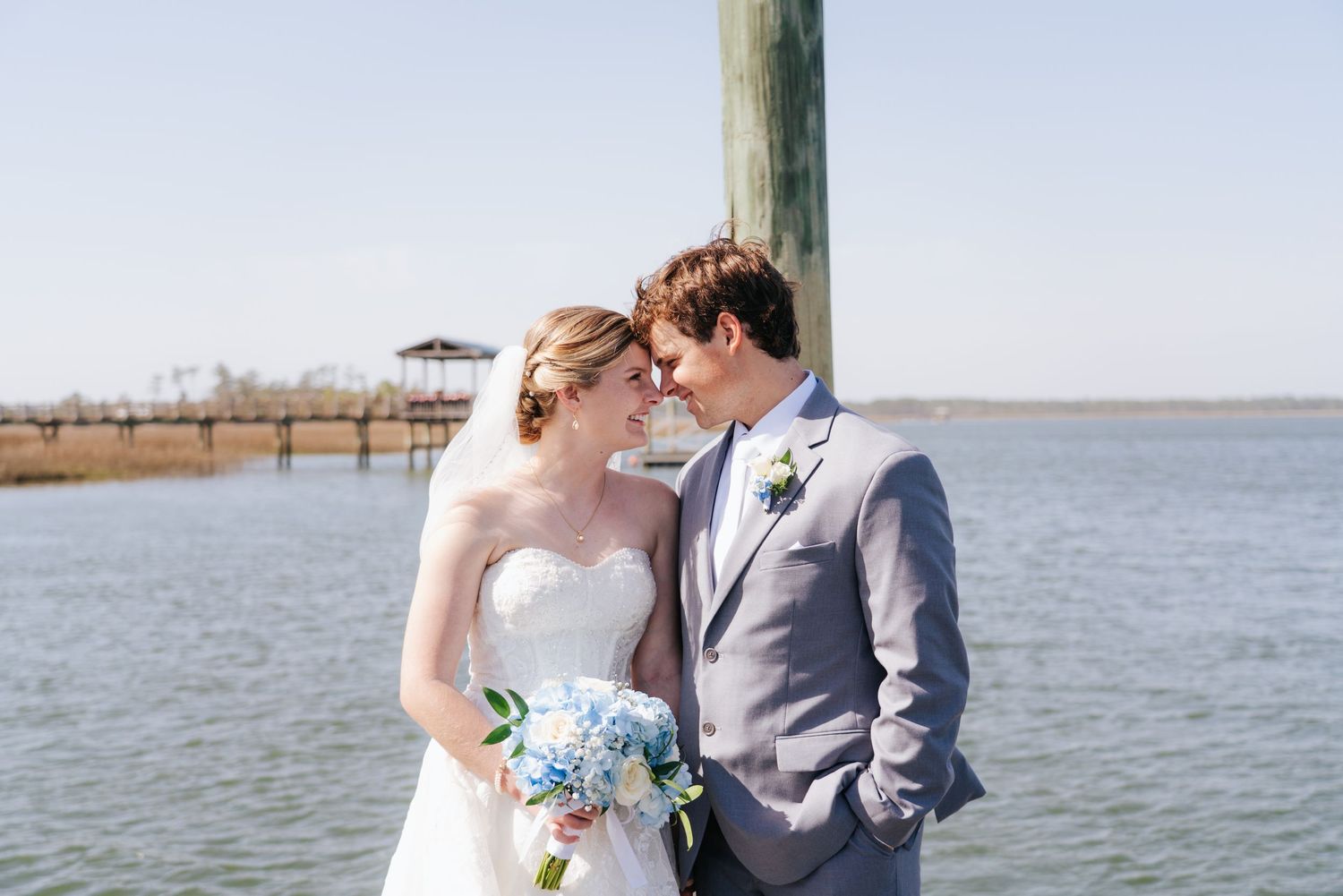 Romantic waterfront wedding ceremony with couple embracing on wooden dock.