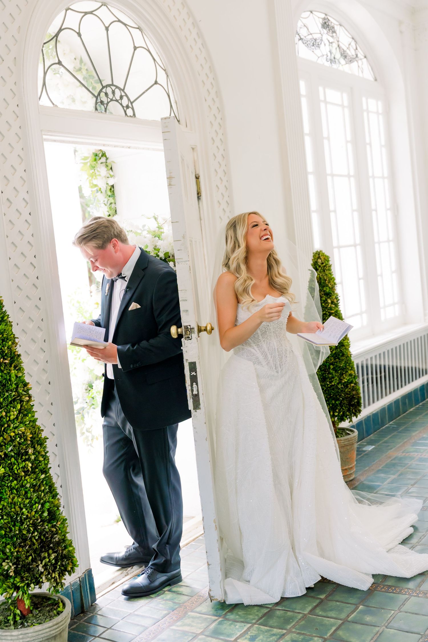 Bride and groom share emotional private vows reading moment in elegant white doorway before wedding ceremony.