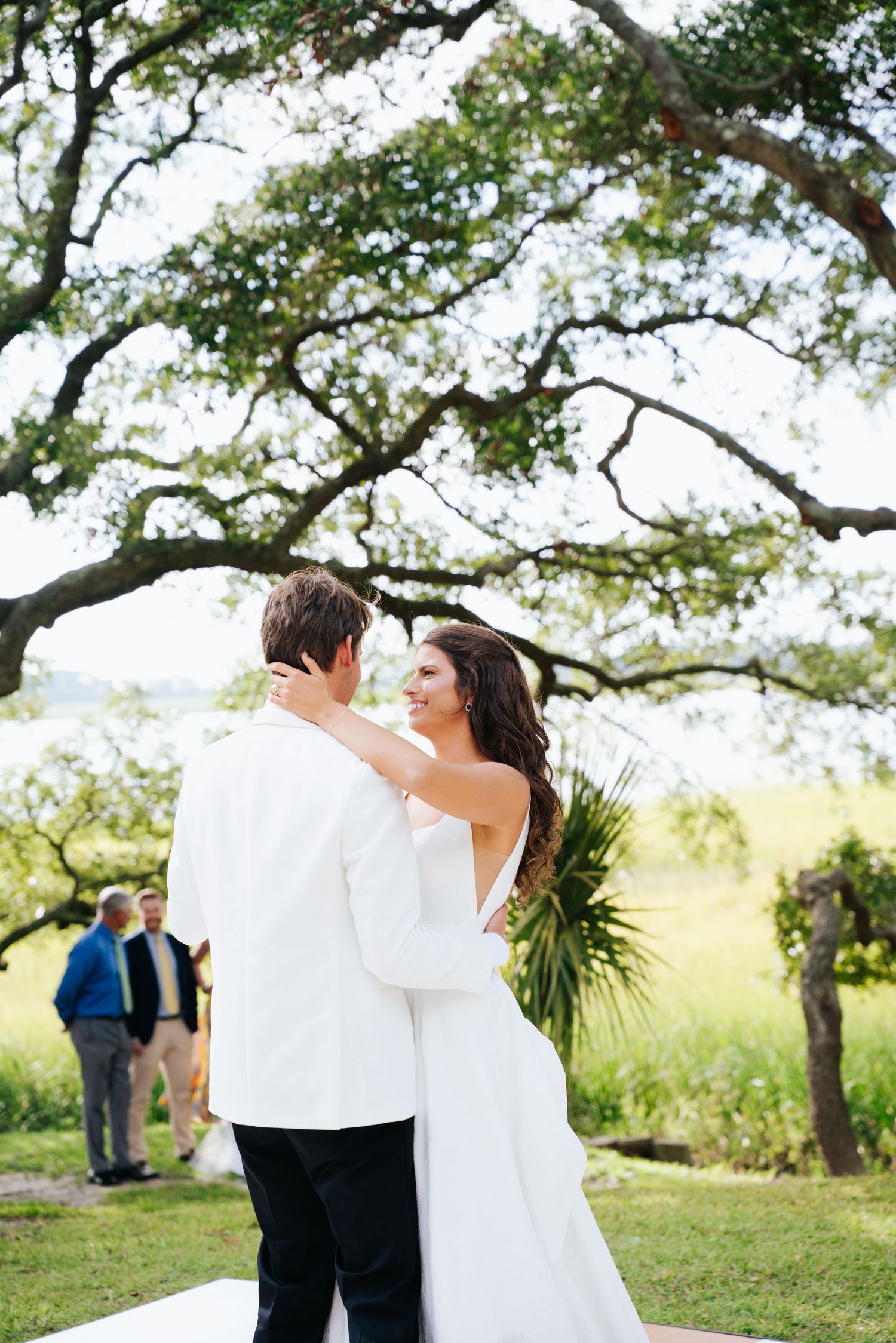 Wedding couple dancing outdoors under oak trees in a scenic marsh setting.