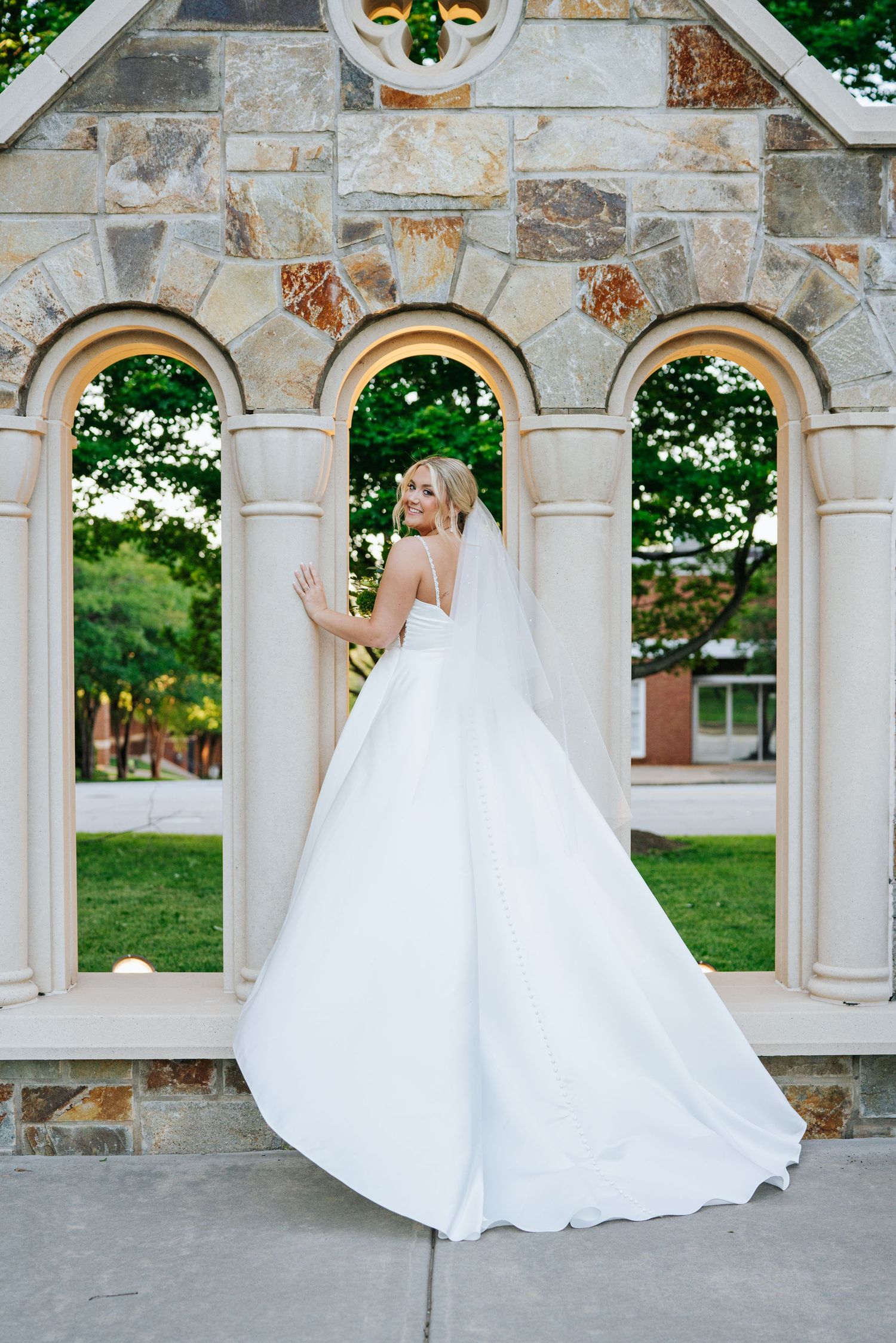 A bride in a ballgown poses under stone arches with elegant architectural details.